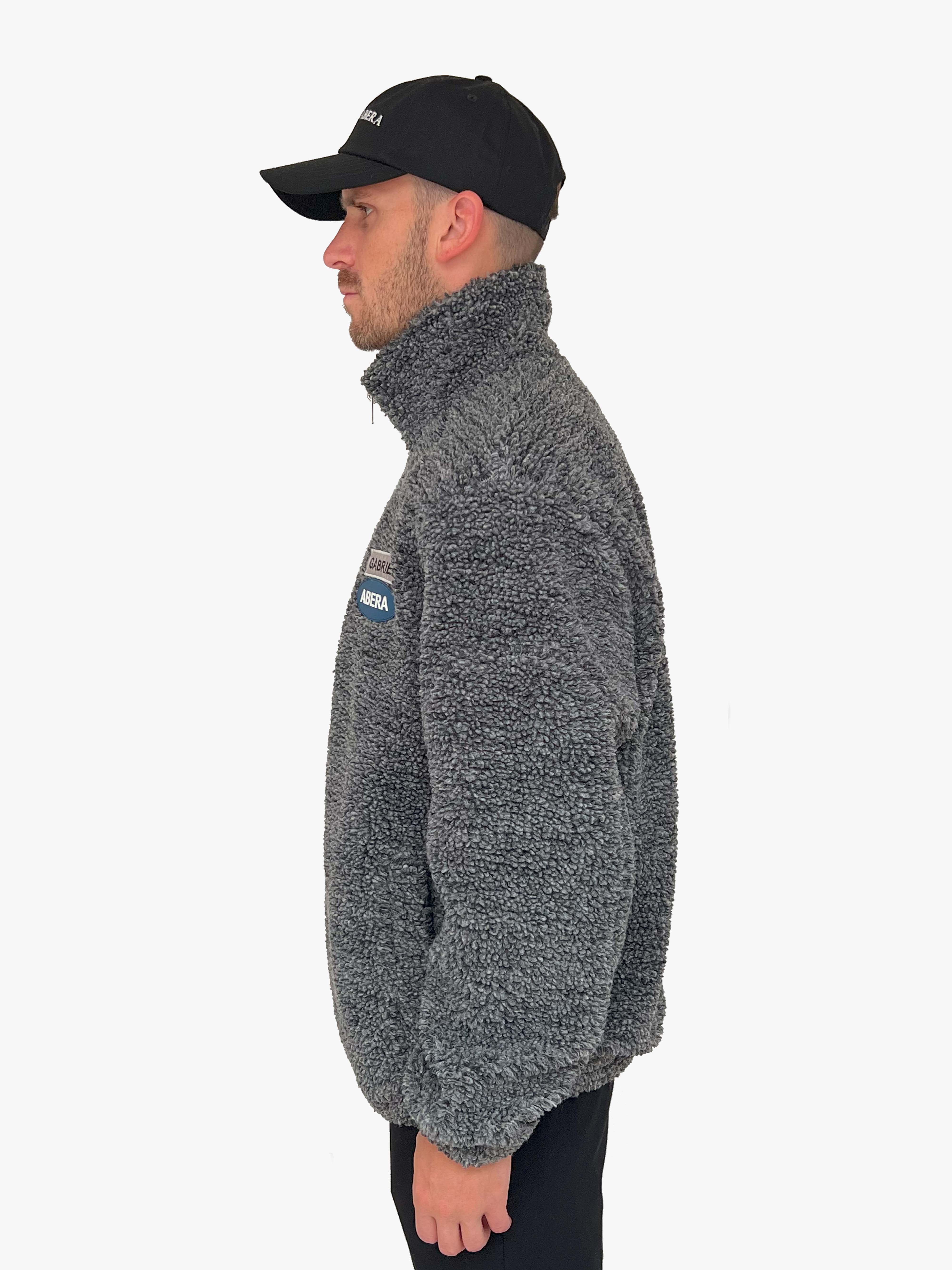 Male model wearing a black fleece jacket with grey and blue brand patches