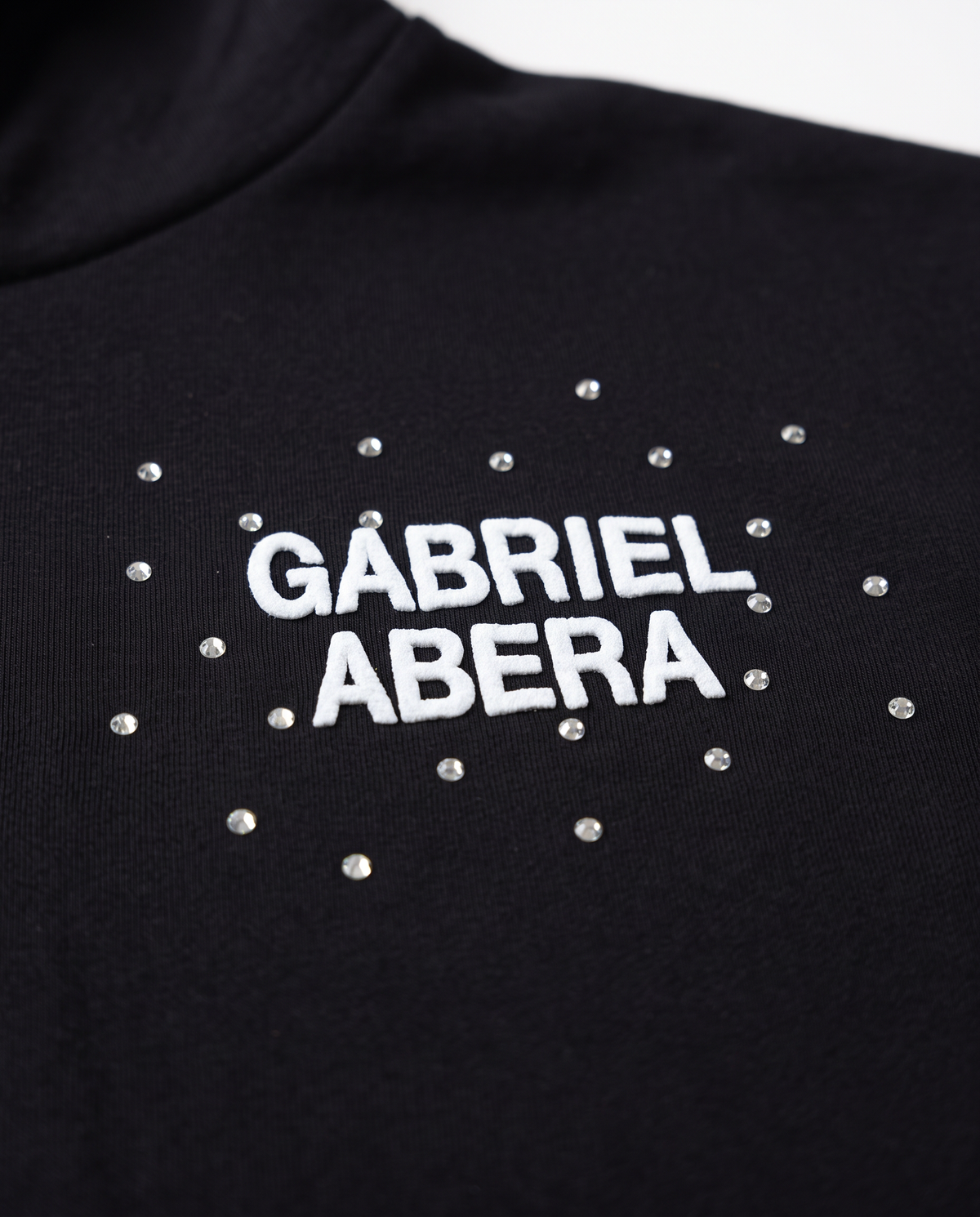 Nahaufnahme des GABRIEL ABERA Logos und der handgesetzten Rhinestones und Strasssteine auf dem schwarzen Astral Hoodie
