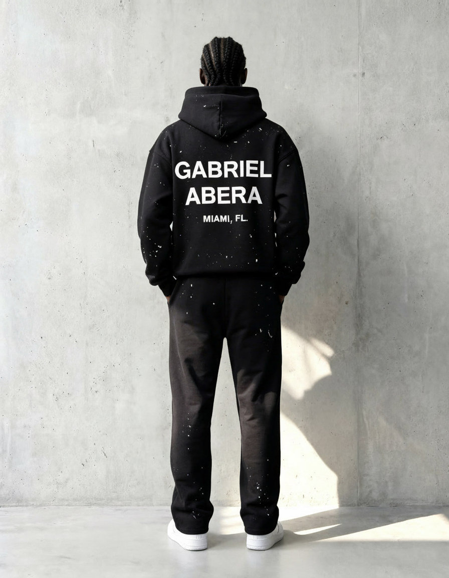 back view of black paint splatter hoodie worn by model, full body, GABRIEL ABERA logo and exact hoodie design clearly visible, clean studio background