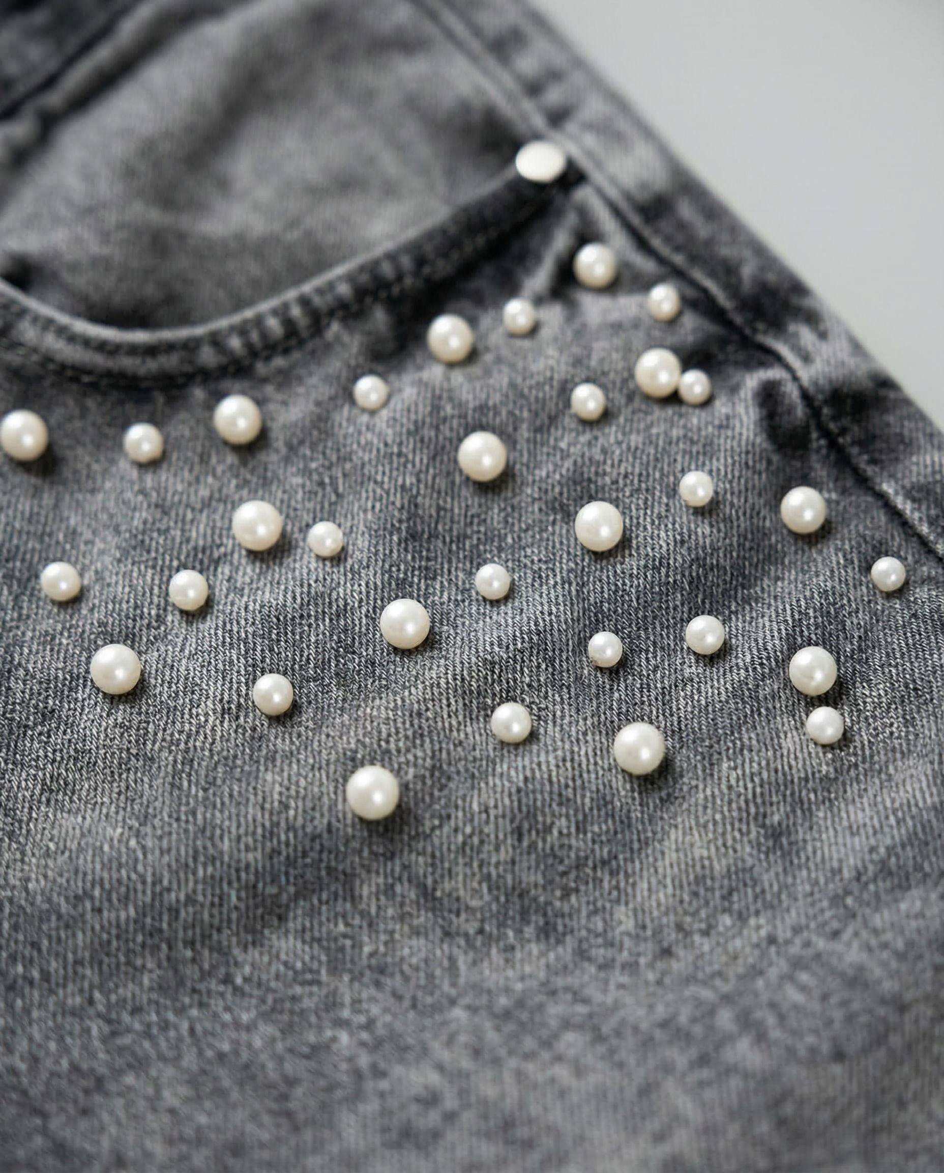 Detailed view of pearls embellishments on the front pocket of GABRIEL ABERA grey rhinestone denim jeans.