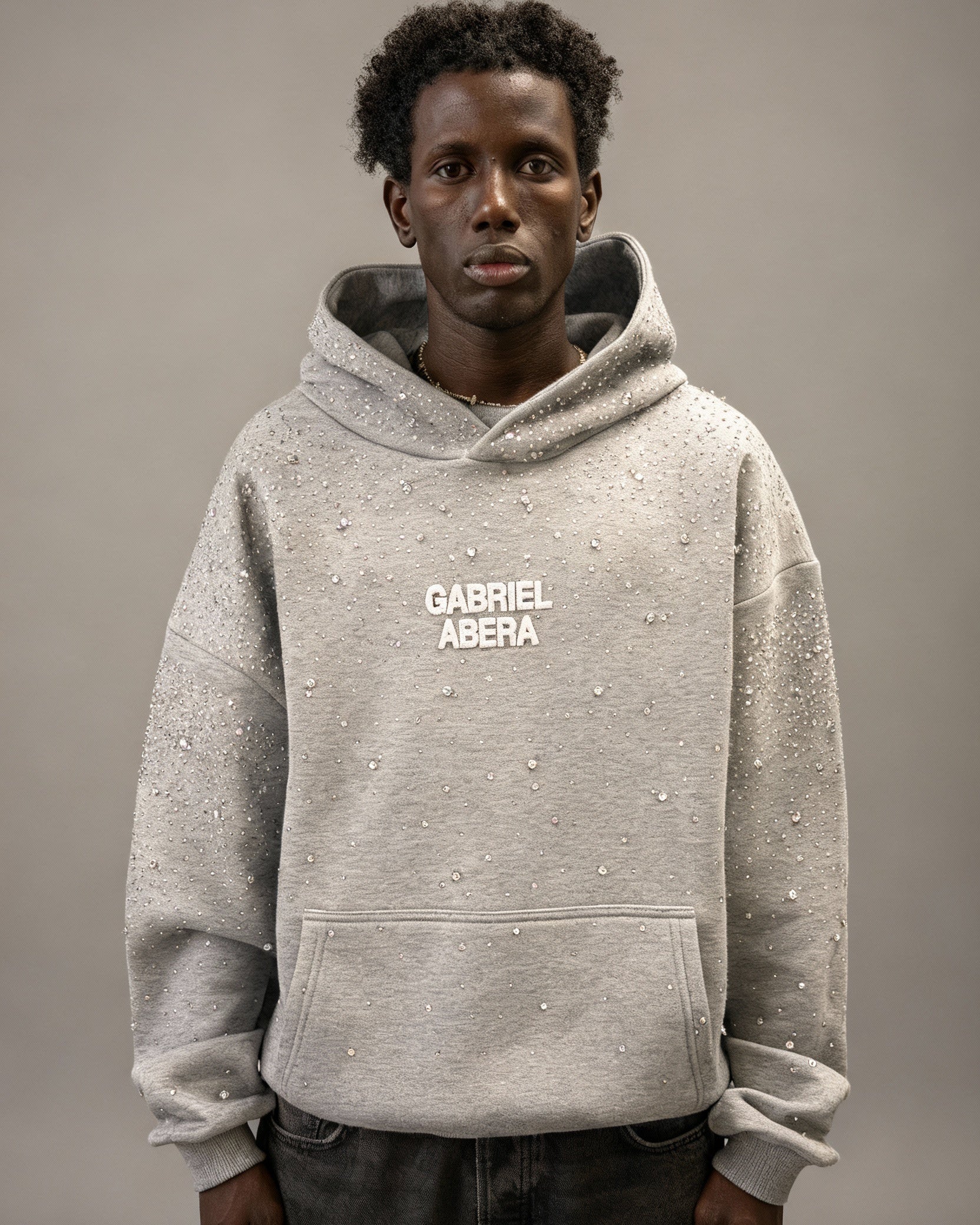 Männliches Model trägt grauen GABRIEL ABERA Universe Hoodie mit handgesetzten Rhinestones – Frontansicht im Oversized Streetwear Fit.