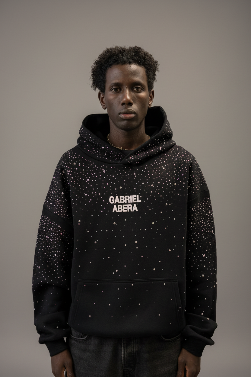Männliches Model trägt schwarzen GABRIEL ABERA Rhinestone Hoodie – Frontansicht, handgesetzte Rhinestones sichtbar, oversized Streetwear Look.