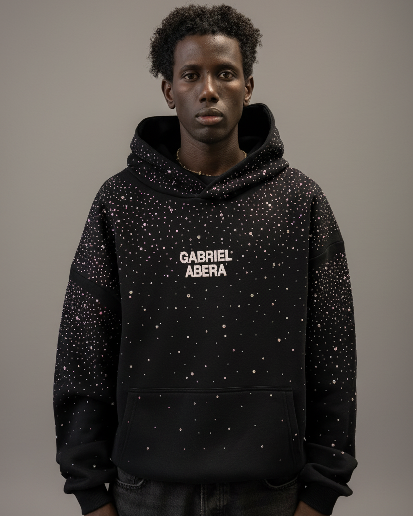 Männliches Model trägt schwarzen GABRIEL ABERA Rhinestone Hoodie – Frontansicht, handgesetzte Rhinestones sichtbar, oversized Streetwear Look.