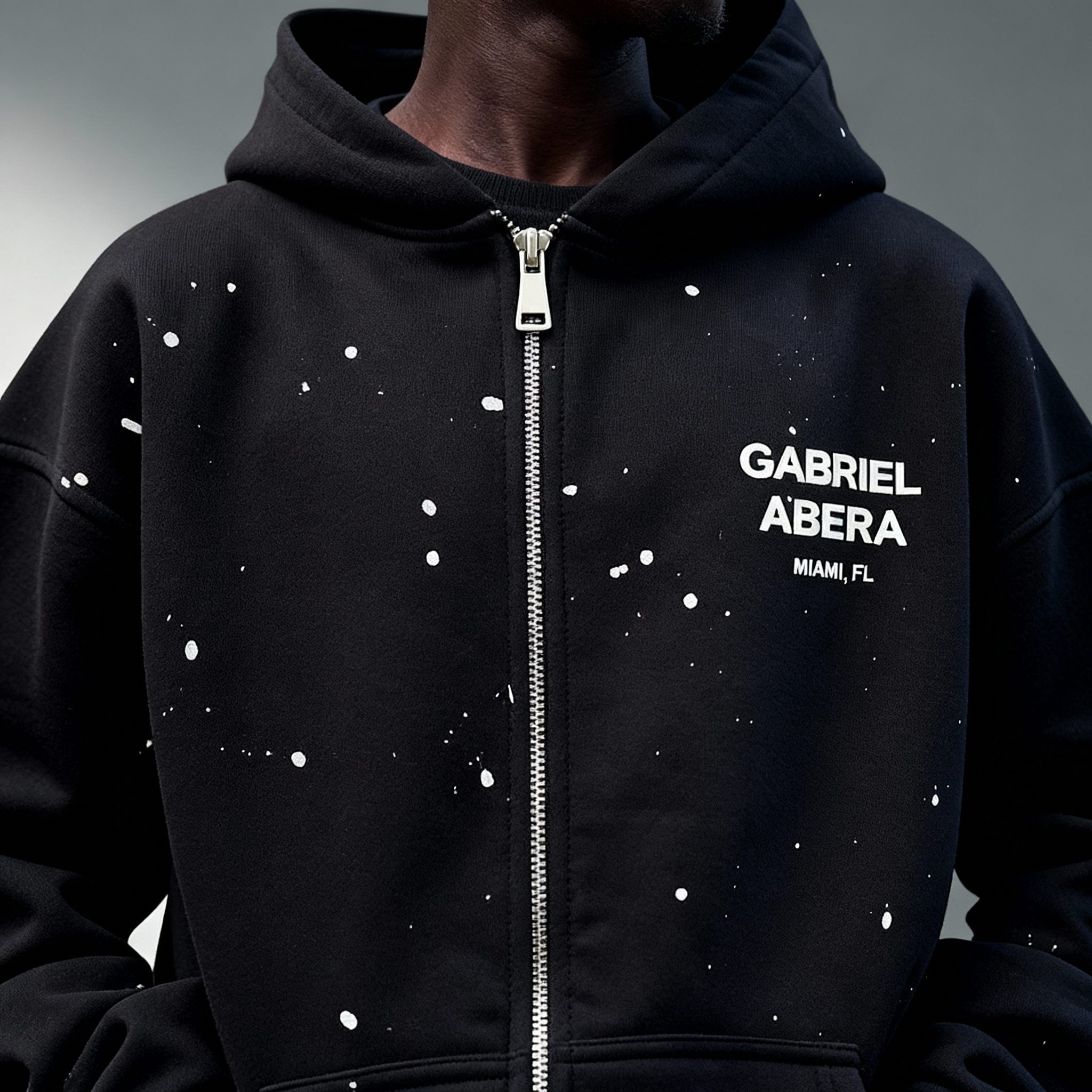 Model trägt GABRIEL ABERA Splattered Puff Hoodie Black/White – Seitenansicht, lockerer Oversized Fit und künstlerisches Paint Splatter Design. Puff-Print Detail des GABRIEL ABERA Splattered Puff Hoodie und Pants im Set.