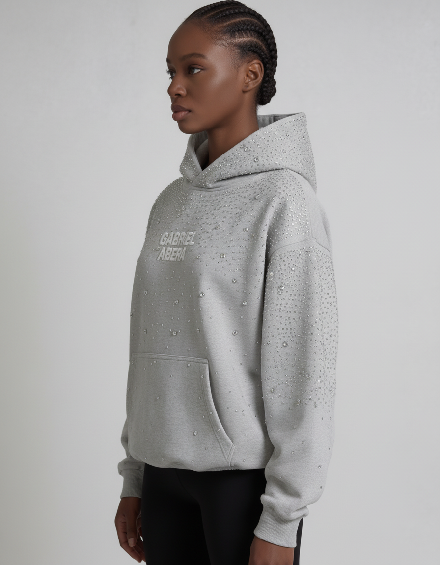 Grauer GABRIEL ABERA Universe Hoodie – weibliches Model seitlich fotografiert, Oversized Silhouette mit funkelnden Rhinestones sichtbar.