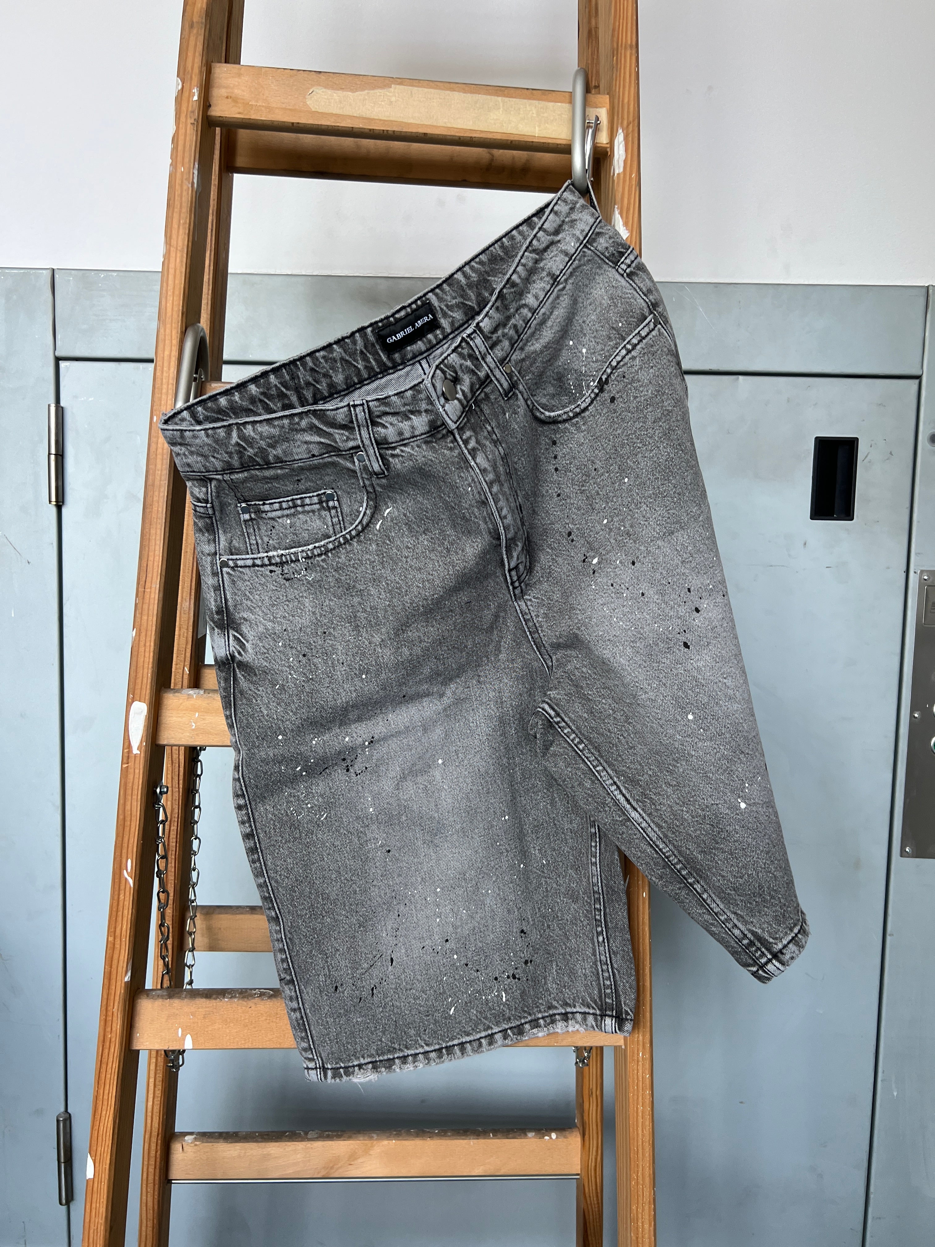 Gabriel Abera Splattered Denim Jorts draped over ladder, washed grey with paint splatter