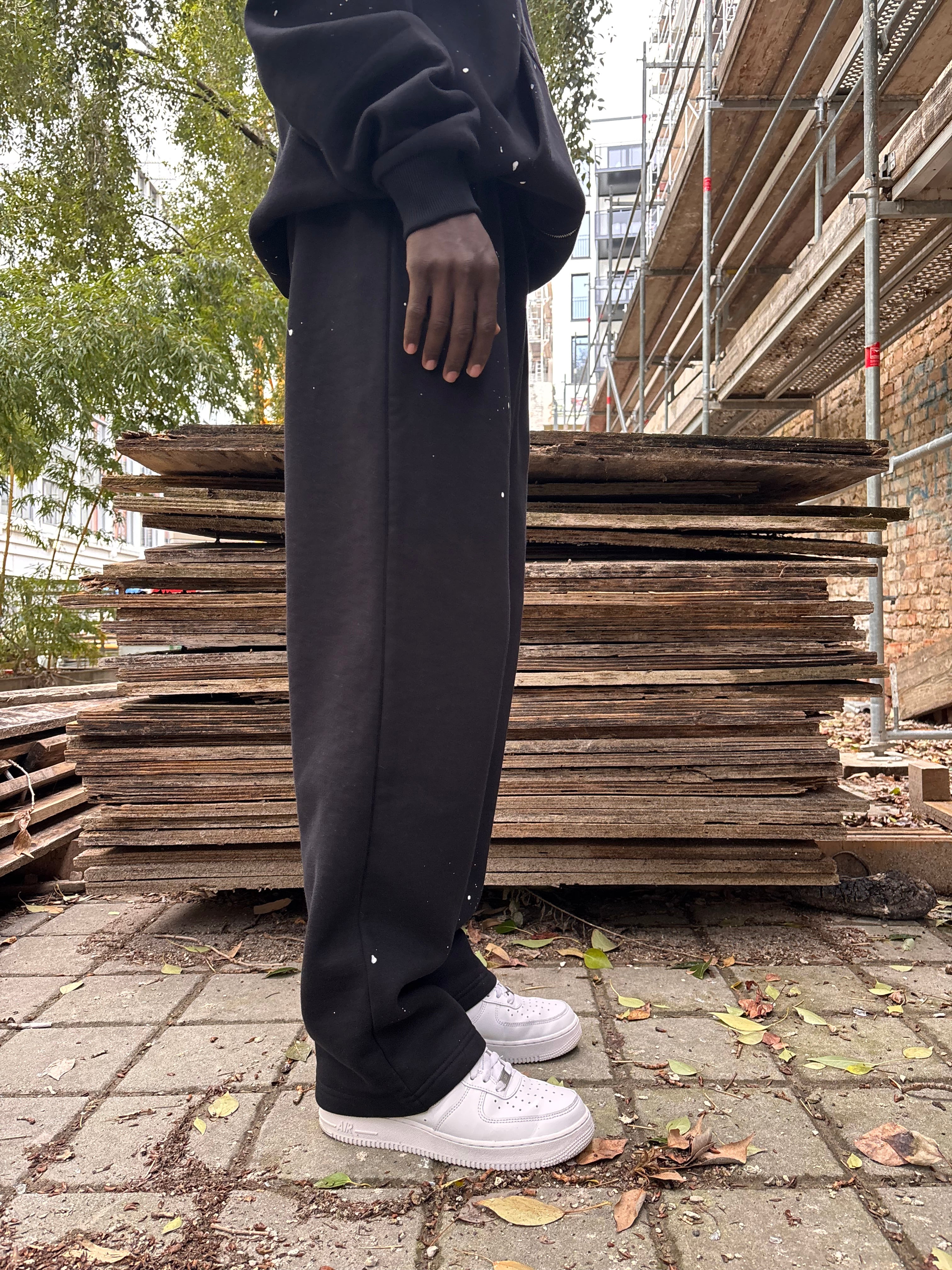 Seitenansicht: Model trägt GABRIEL ABERA Splattered Sweatpants Black/White im Set mit passenden Oberteilen, Oversized Fit mit Splatter-Effekt.