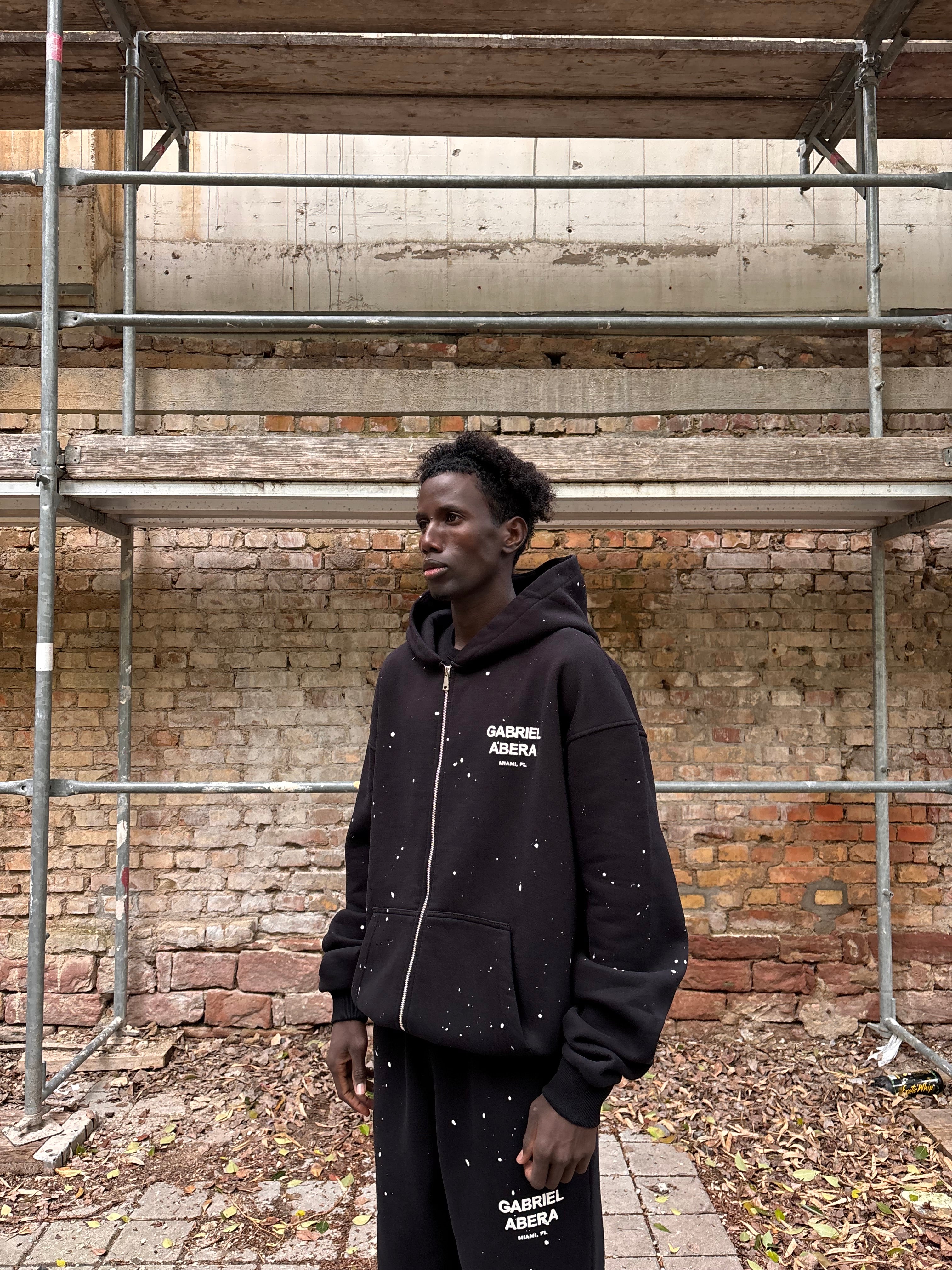 Model trägt GABRIEL ABERA Splattered Puff Zip Hoodie Black/White – Seitenansicht, lockerer Fit, Farbspritzer