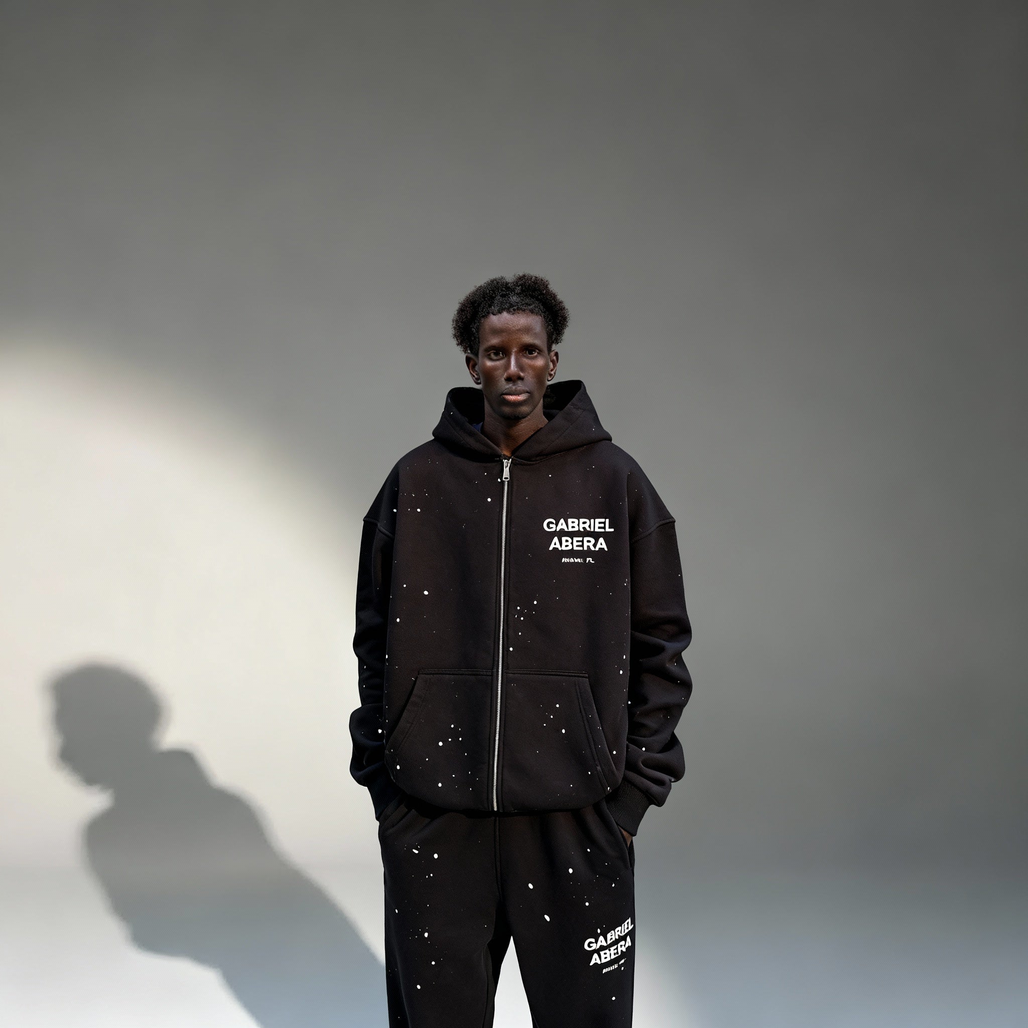 Model trägt GABRIEL ABERA Splattered Puff Zip Hoodie Black/White – Frontansicht, Reißverschluss offen/loss.