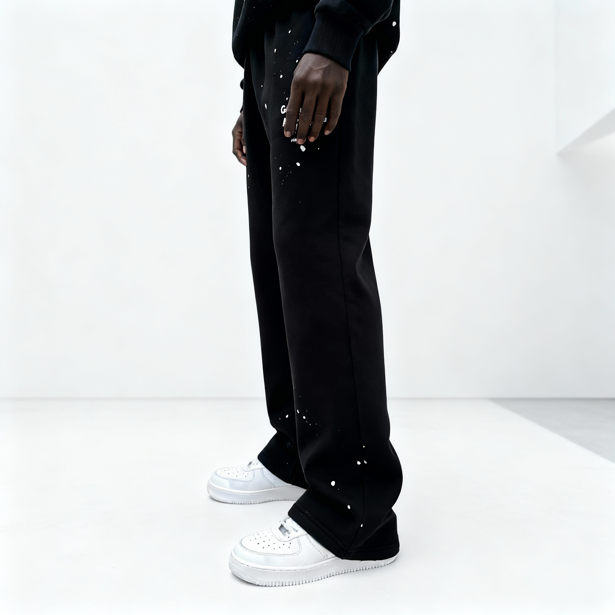 Seitenansicht: Model trägt GABRIEL ABERA Splattered Sweatpants Black/White im Set mit passenden Oberteilen, Oversized Fit mit Splatter-Effekt.