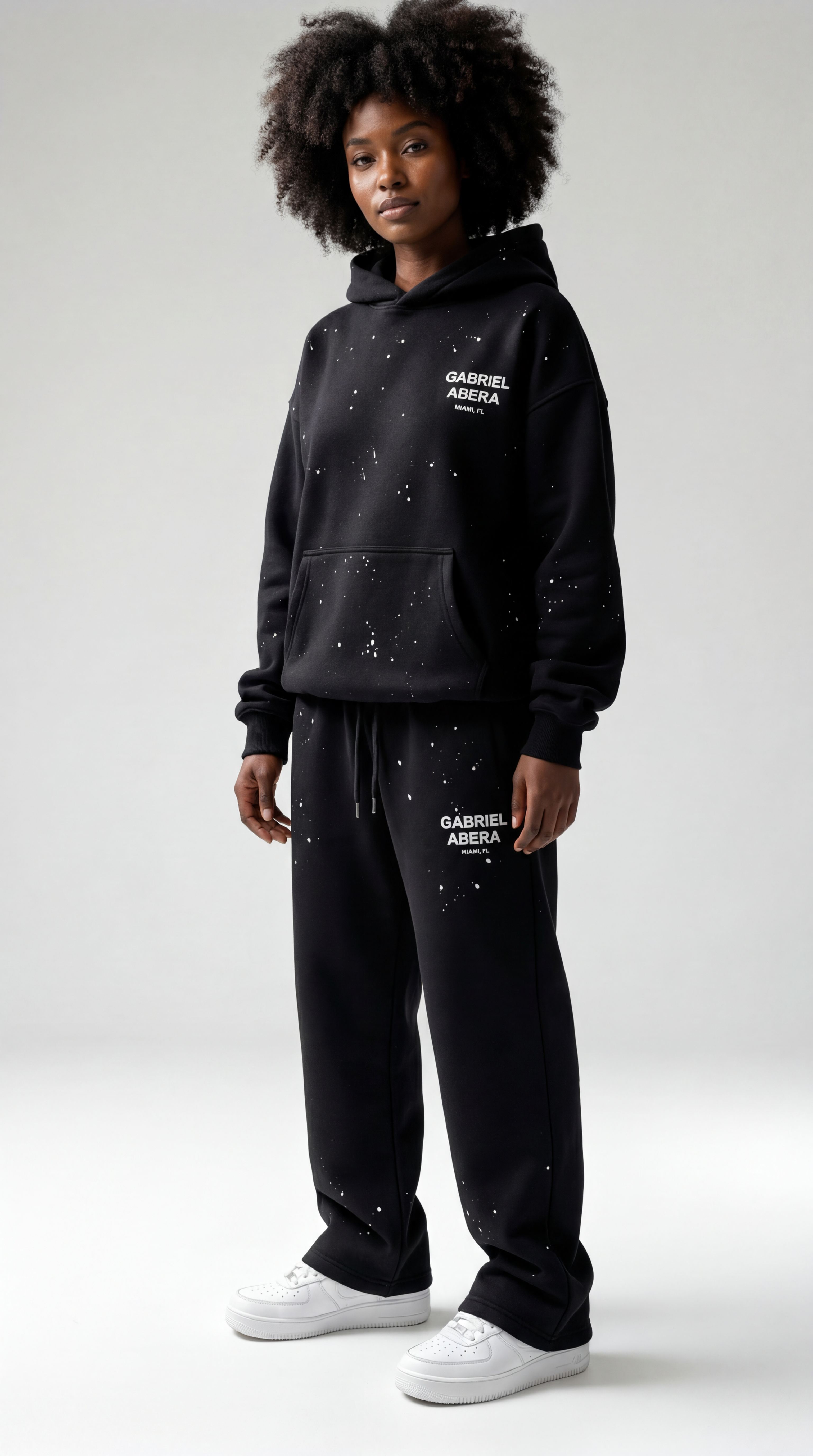 Schwarzes weibliches Model trägt die GABRIEL ABERA Splattered Pants in Schwarz im Oversized Streetwear Fit, Frontansicht.