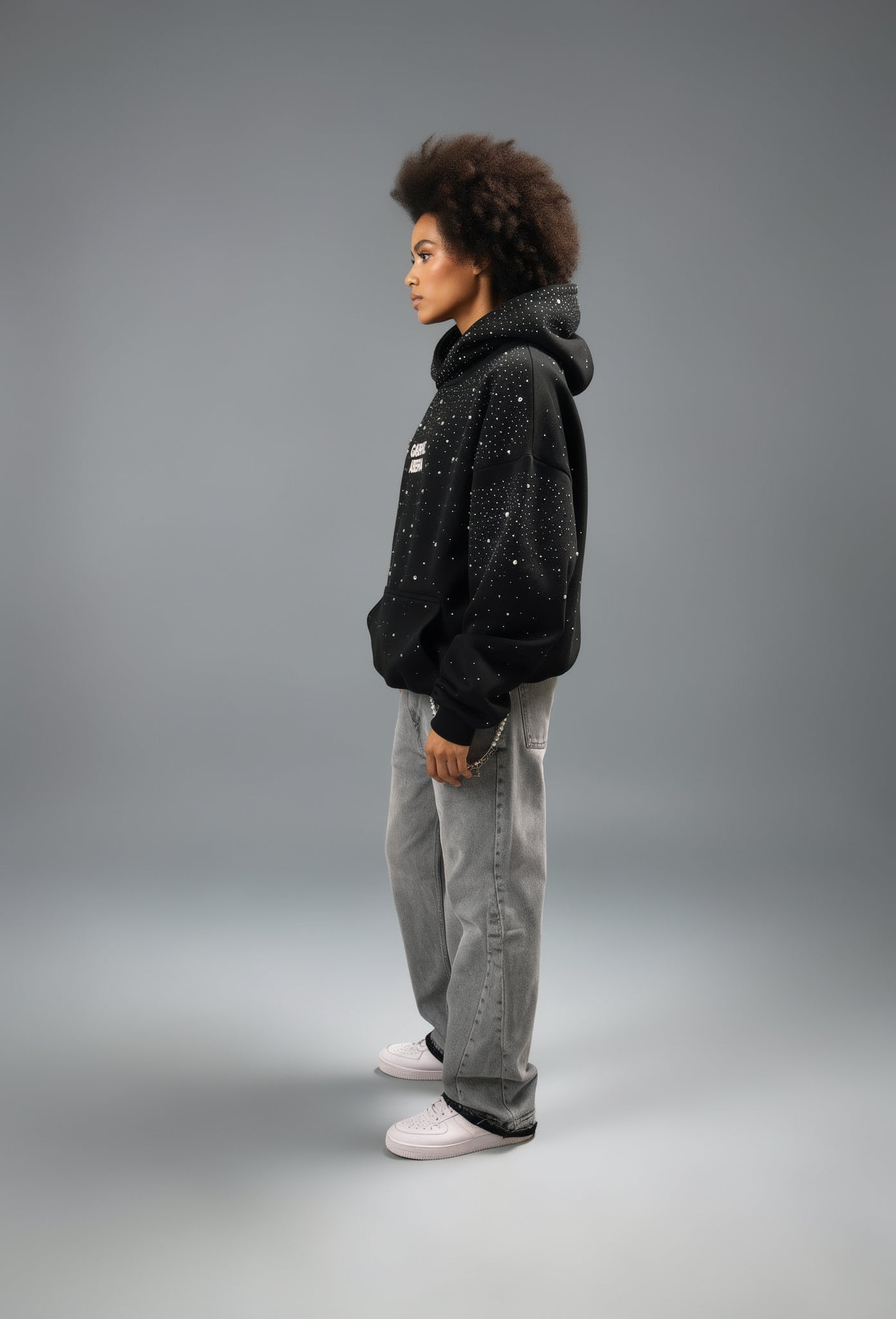 Weibliches Model im kompletten Look – schwarzer GABRIEL ABERA Rhinestone Hoodie im Ganzkörperformat seitlich aufgenommen, urbaner Streetwear Style.