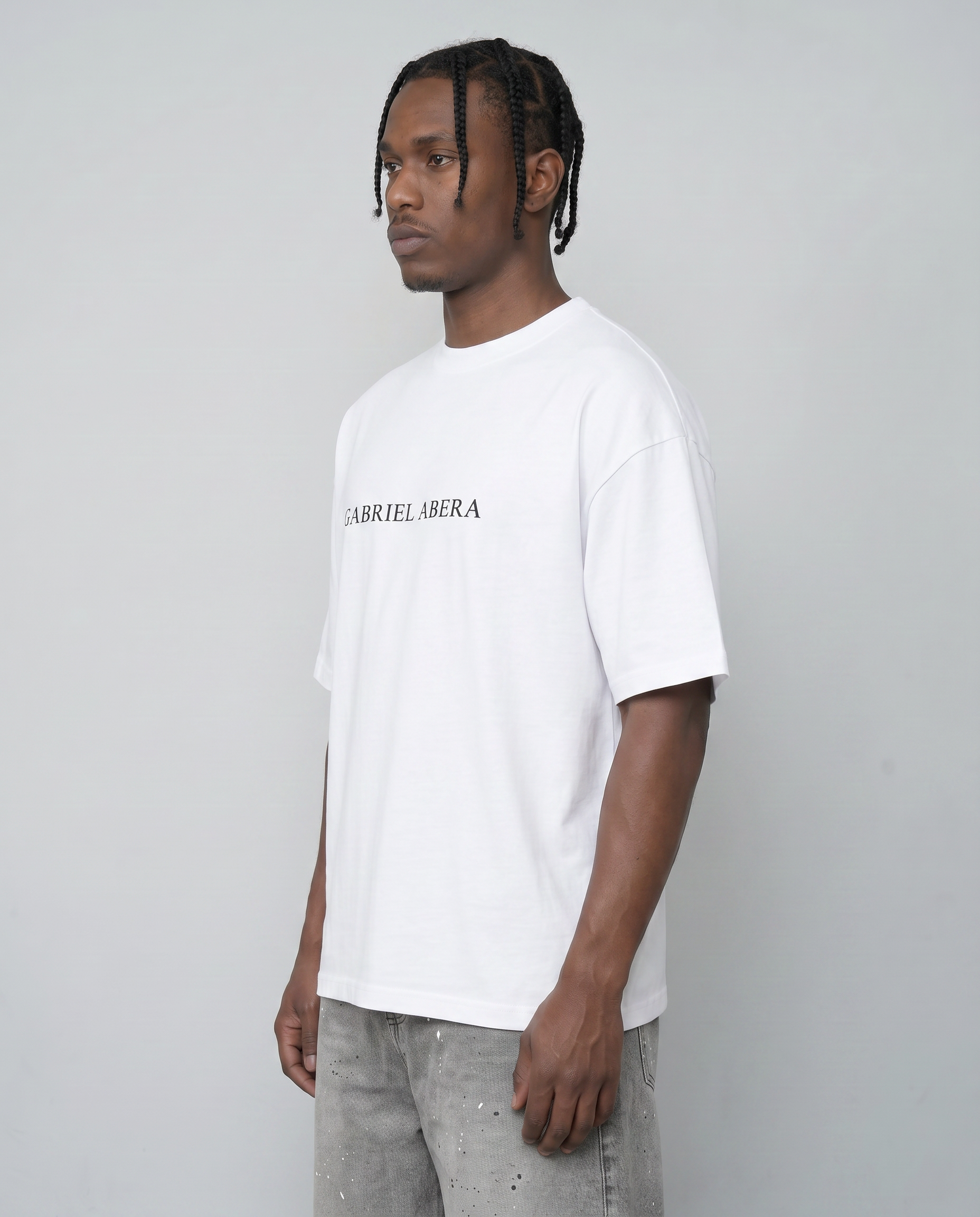Side view male model wearing cream white oversized GABRIEL ABERA t-shirt showing dropped shoulder and loose silhouette