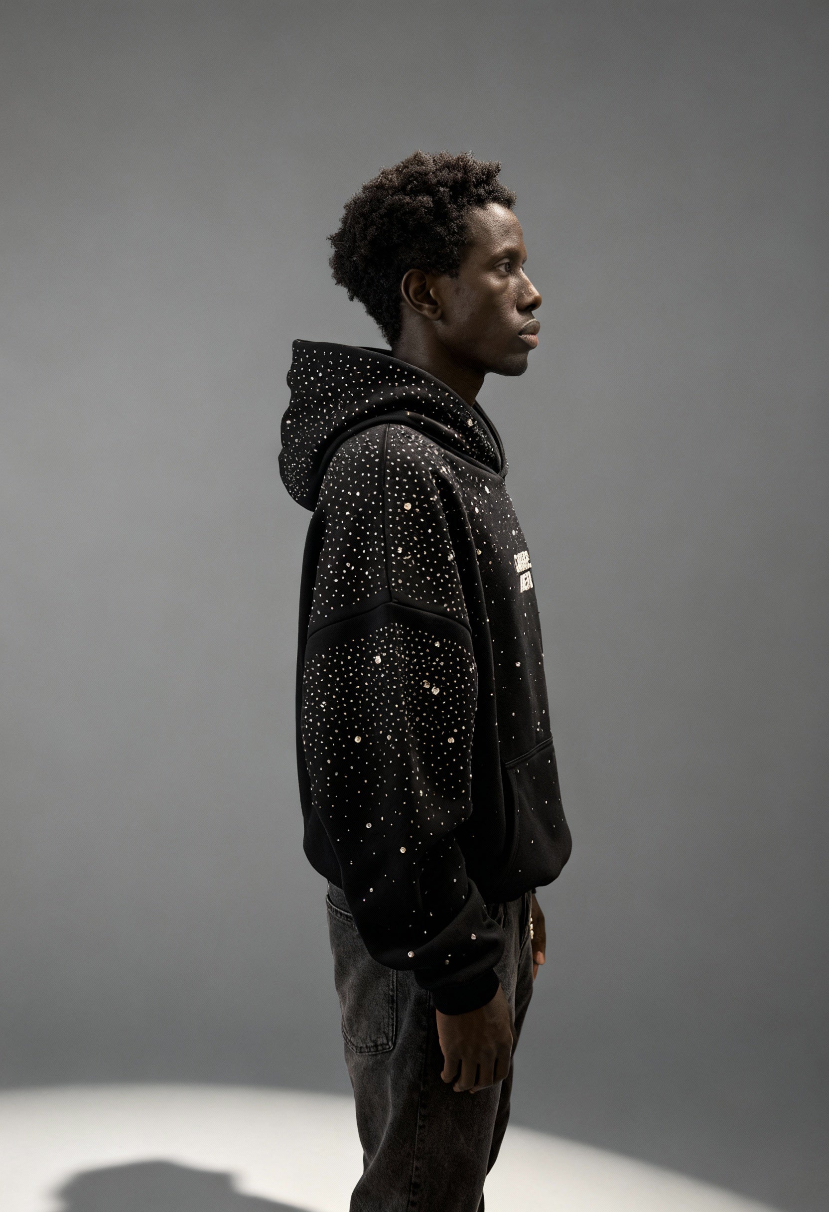 Schwarzer GABRIEL ABERA Rhinestone Hoodie – männliches Model seitlich fotografiert, relaxed Oversized Silhouette und Rhinestone-Details sichtbar.