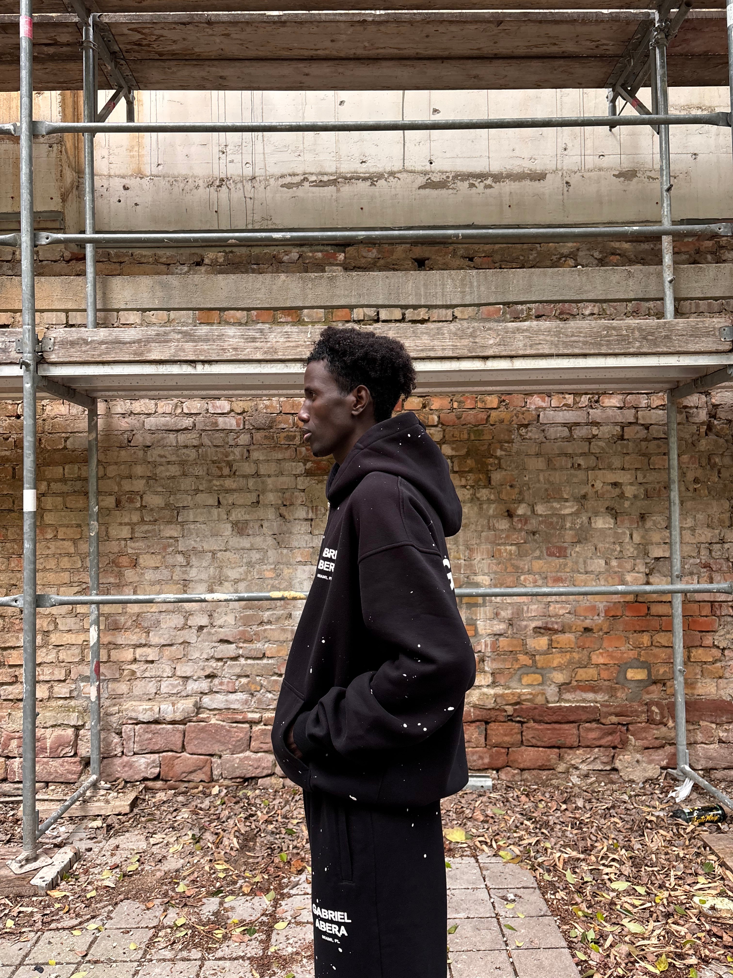Seitenansicht des GABRIEL ABERA Splattered Puff Zip Hoodie Black/White – Oversized Fit mit Hand-Splatter Details.