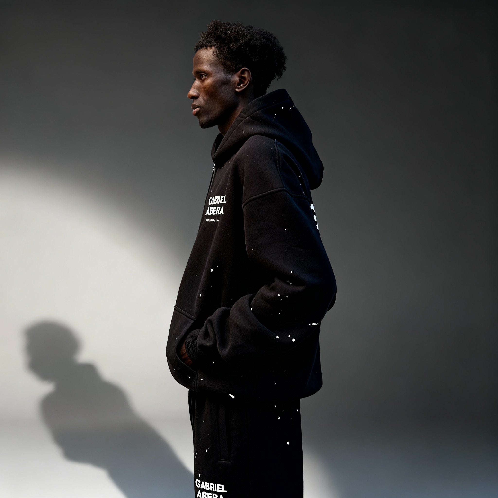 Seitenansicht des GABRIEL ABERA Splattered Puff Zip Hoodie Black/White – Oversized Fit mit Hand-Splatter Details.