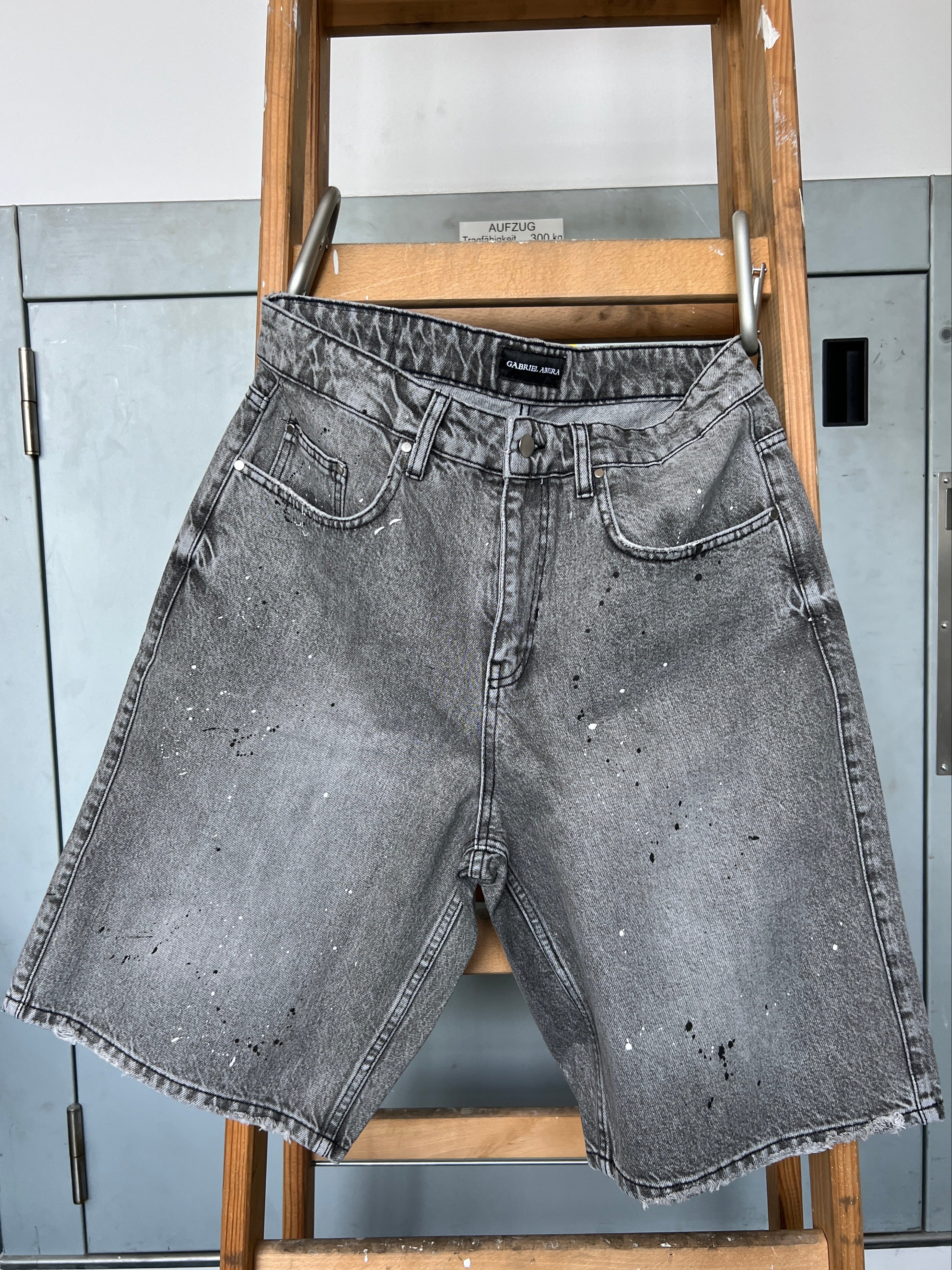 Close-up of paint splatter detail on Gabriel Abera Splattered Denim Jorts hanging on ladder