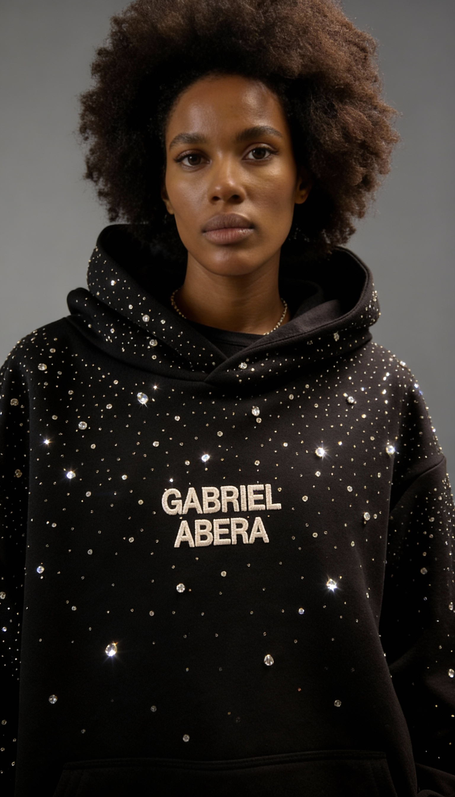 Weibliches Model in schwarzem GABRIEL ABERA Rhinestone Hoodie – Frontansicht, elegante Rhinestone-Applikation, Urban Streetwear Fit.