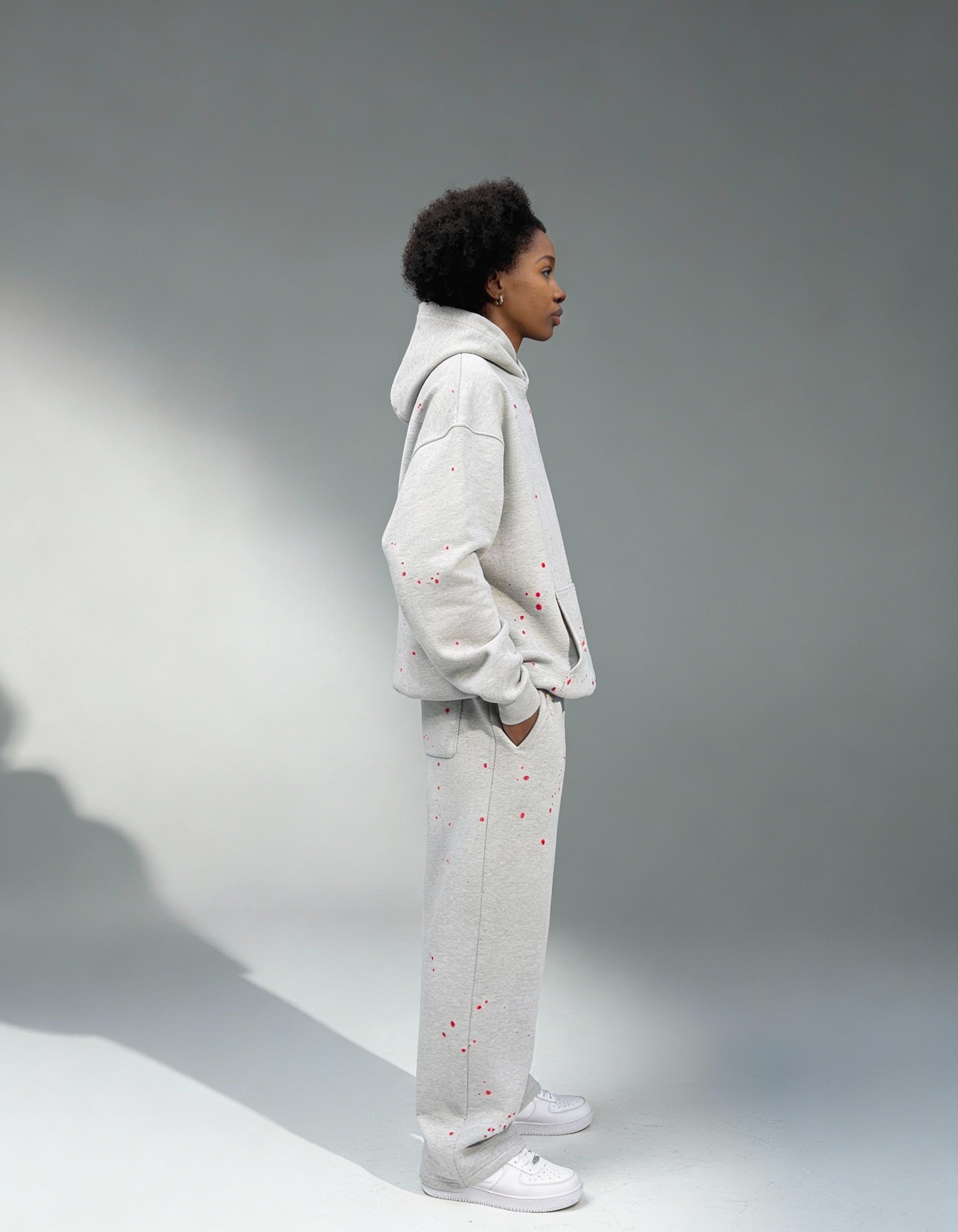 Weibliches Model seitlich fotografiert in der GABRIEL ABERA Splattered Tracksuit mit roten Paint Splatter Akzenten – moderner Urban Fit.
