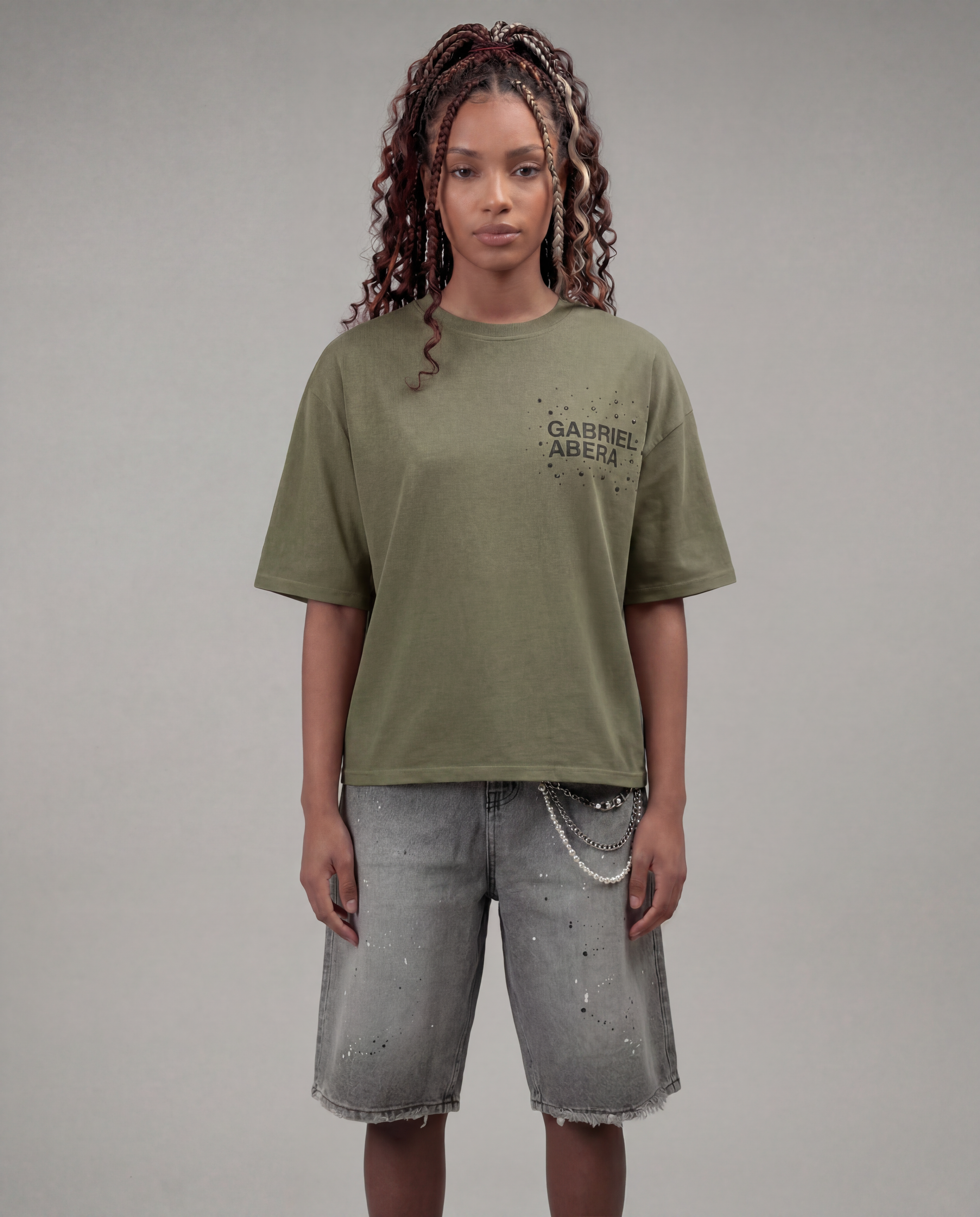 Female model wearing the Gabriel Abera Rhinestone Logo Tee in olive with denim shorts – front view, relaxed oversized fit, grey background