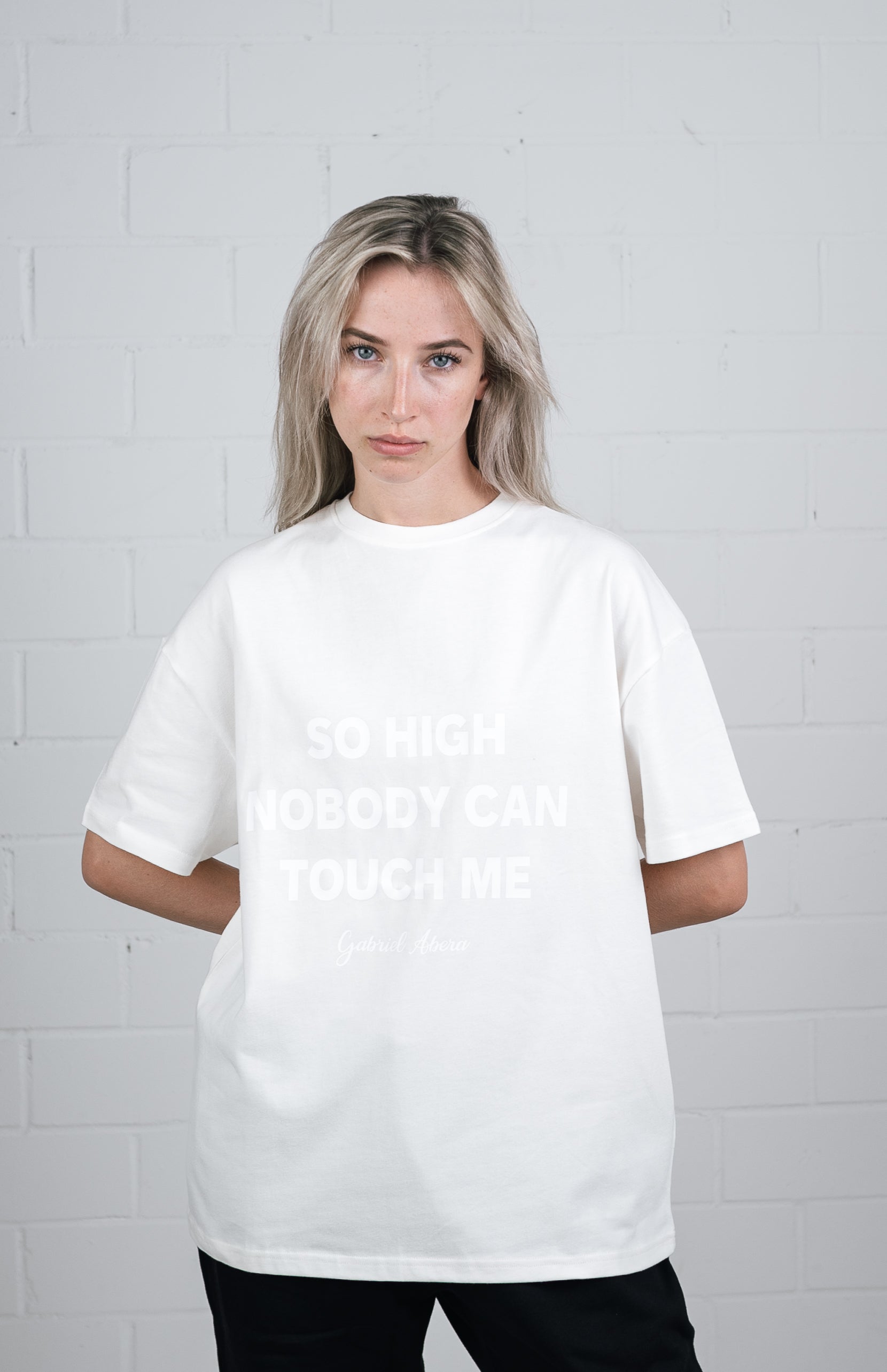 Female model wearing a White oversize tshirt with white so high nobody can touch me design in the front