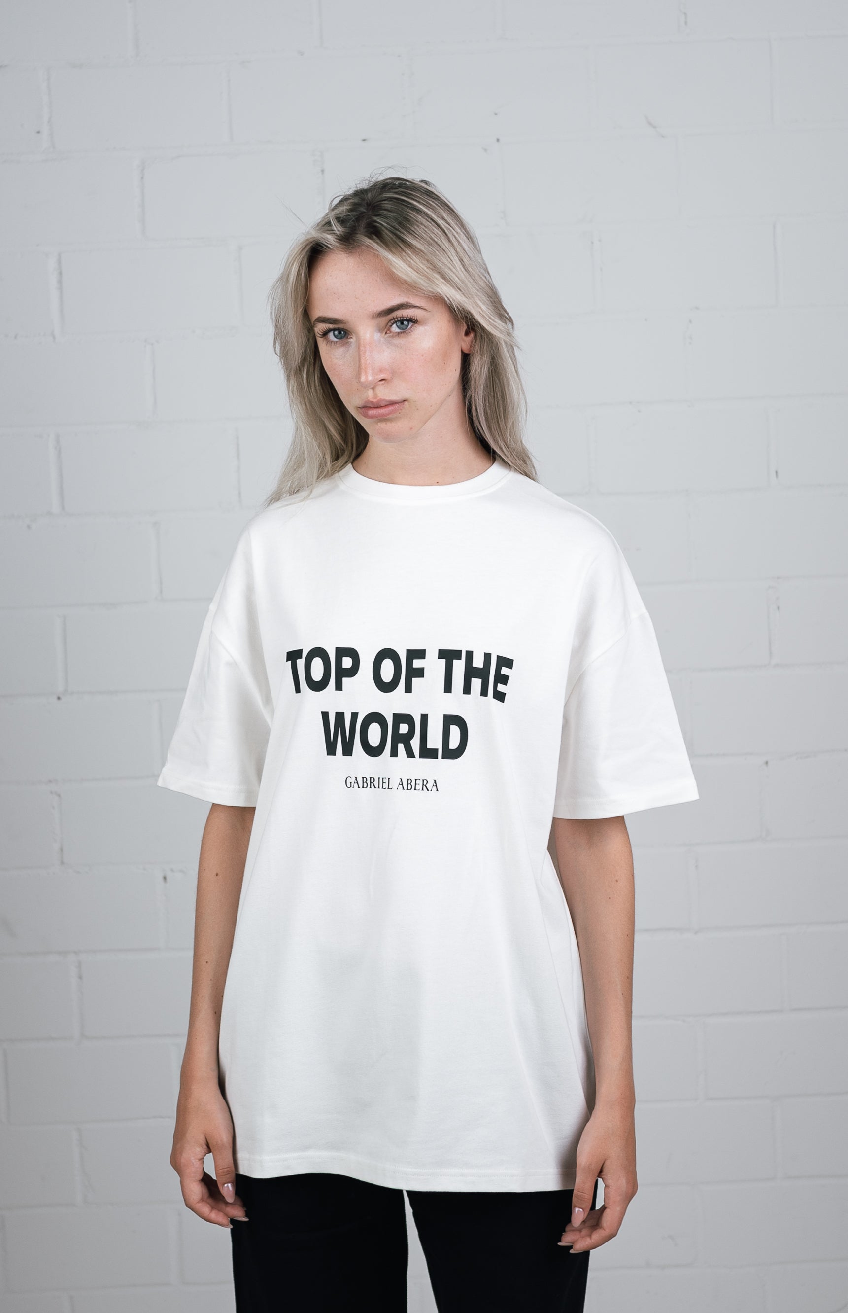 Female model wearing a White oversize tshirt with black top of the world design in the front