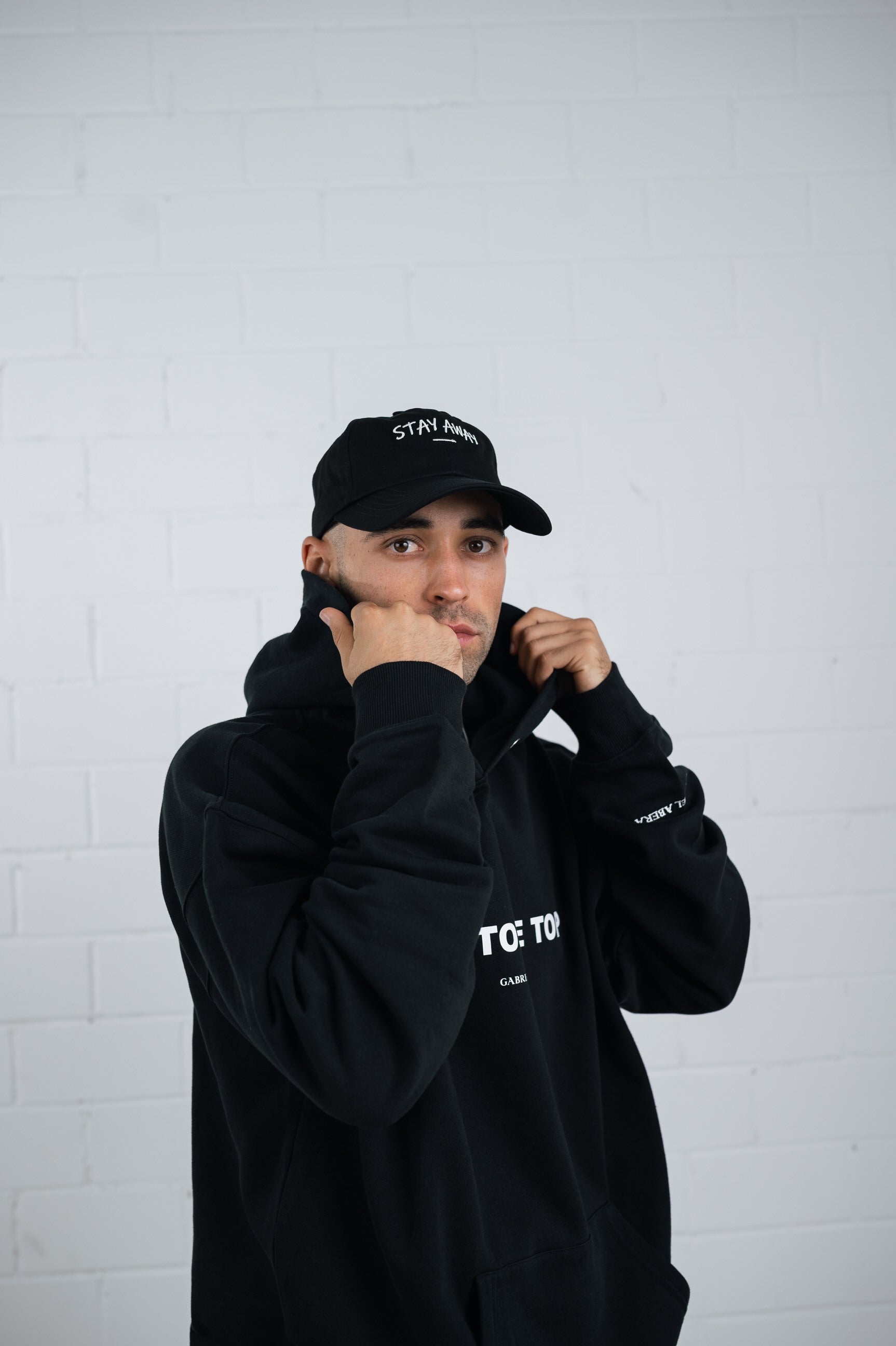 Male model wearing a Black cap with white stay away embroidery