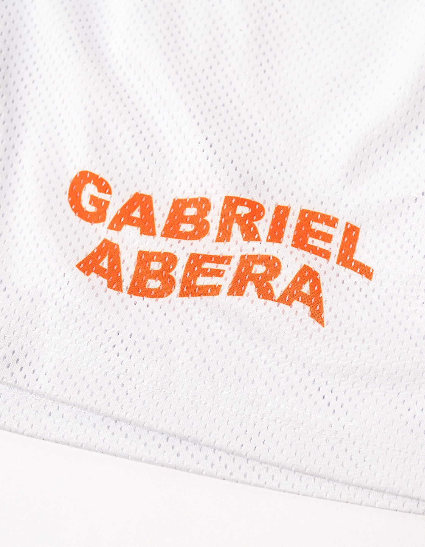 close up of a white mesh shorts with orange brand name print in the front
