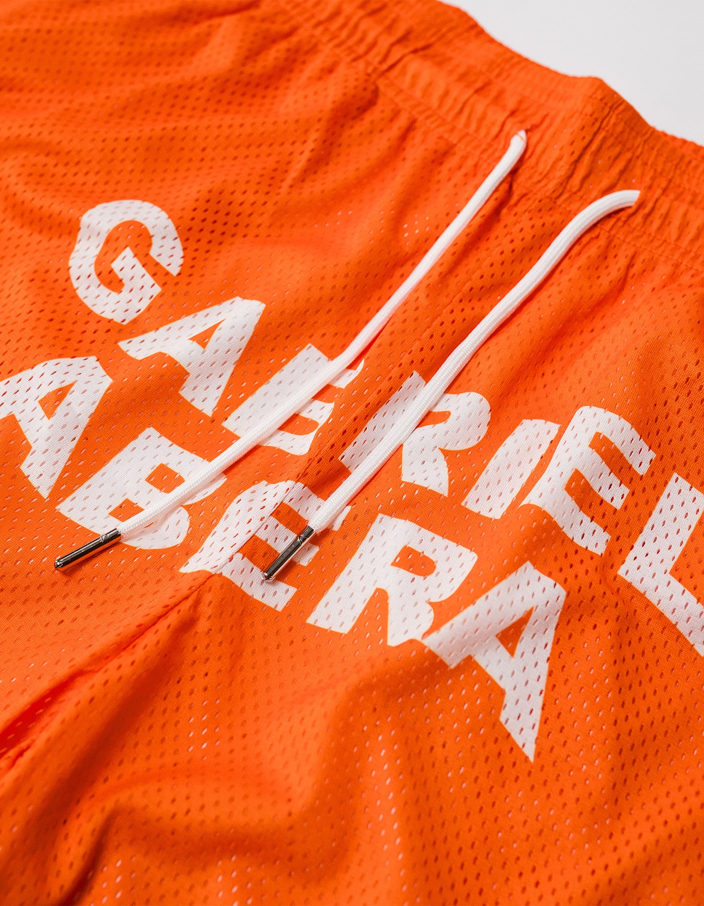close up on a  Orange mesh shorts with white brand name print in the front