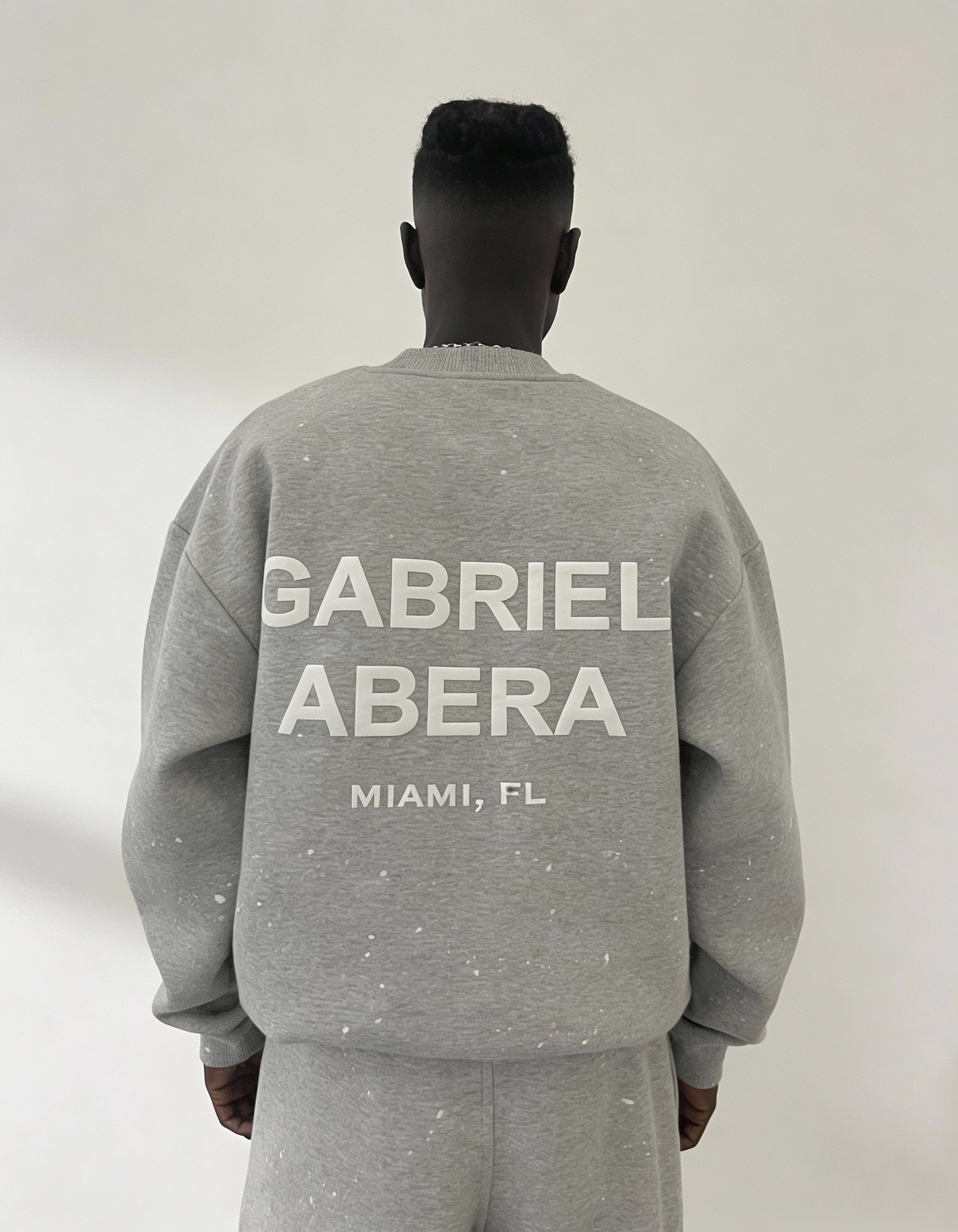 Back view des grauen Splattered Sweaters von GABRIEL ABERA mit relaxed oversized Fit, weißen Puff Print und einzigartigen Paint Splatter Details.
