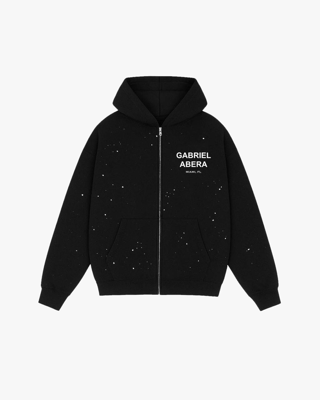 GABRIEL ABERA Splattered Puff Zip Hoodie Black/White – Frontansicht mit Farbspritzern & Puff-Print auf Brust.