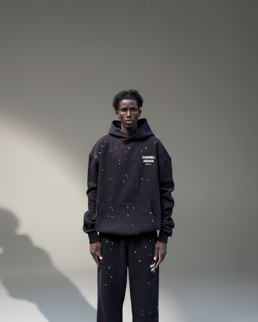 Model trägt GABRIEL ABERA Splattered Puff Hoodie Black/White – Frontansicht, Oversized Fit mit handgemachtem Farbspritzer-Design.