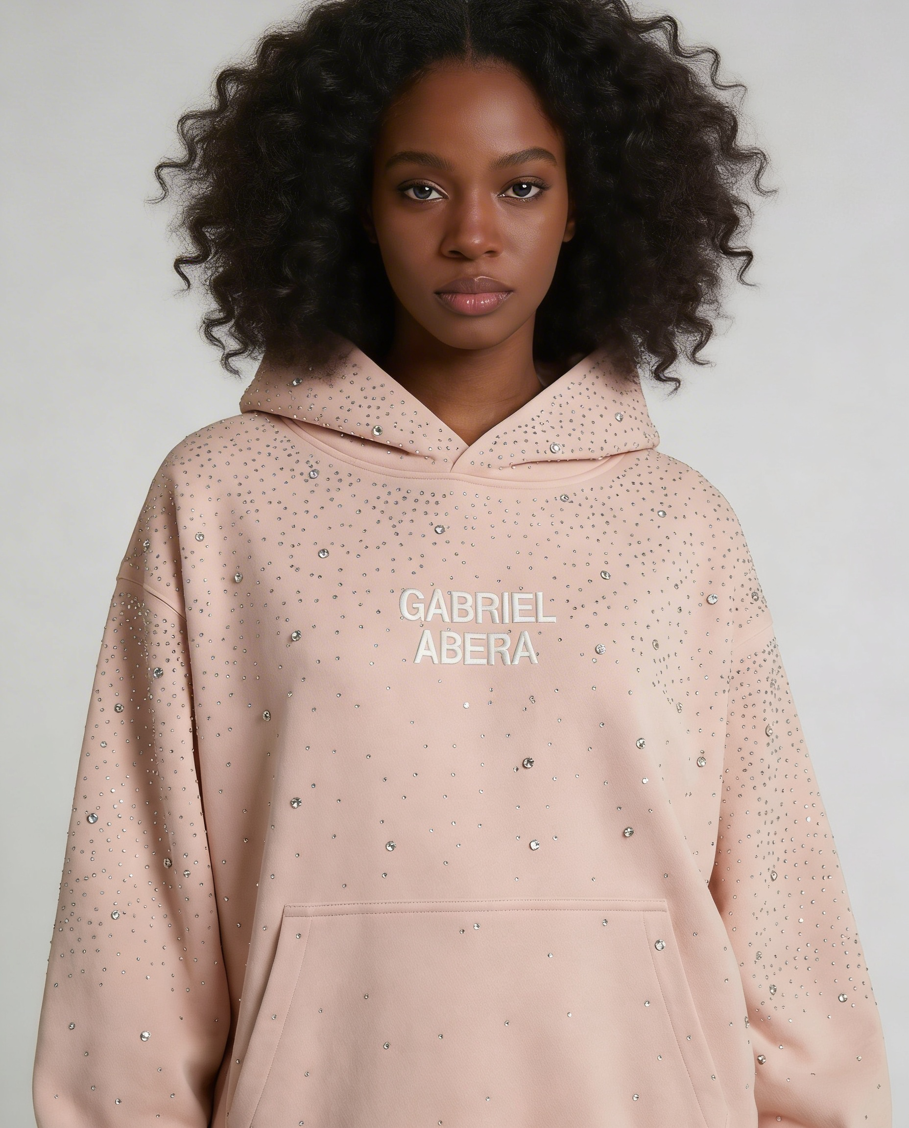Female model wearing pink rhinestone hoodie by GABRIEL ABERA front view oversized unisex fit with hand-applied crystals streetwear