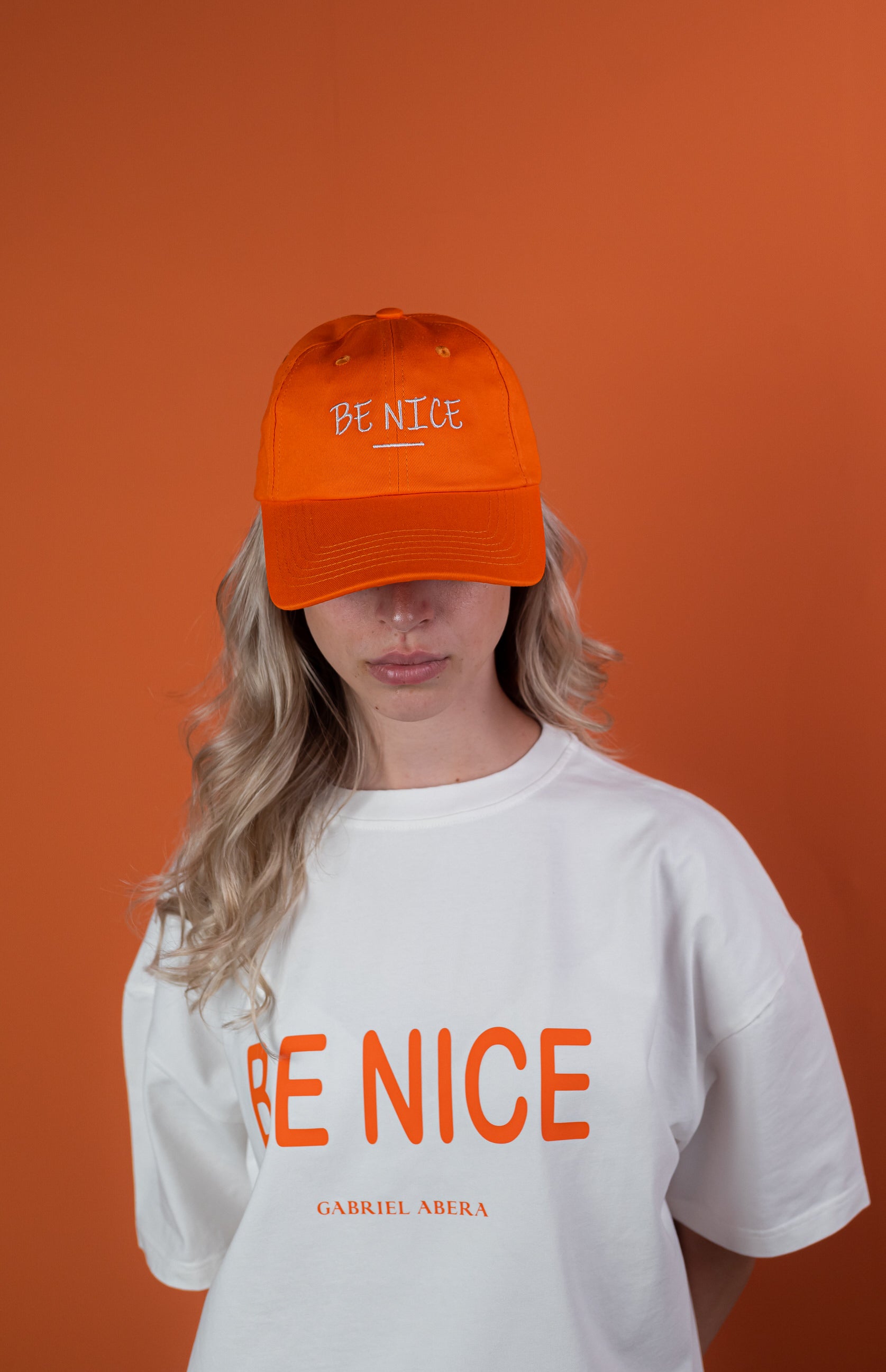 Female Model wearing a Orange cap with "be nice" writing on the front