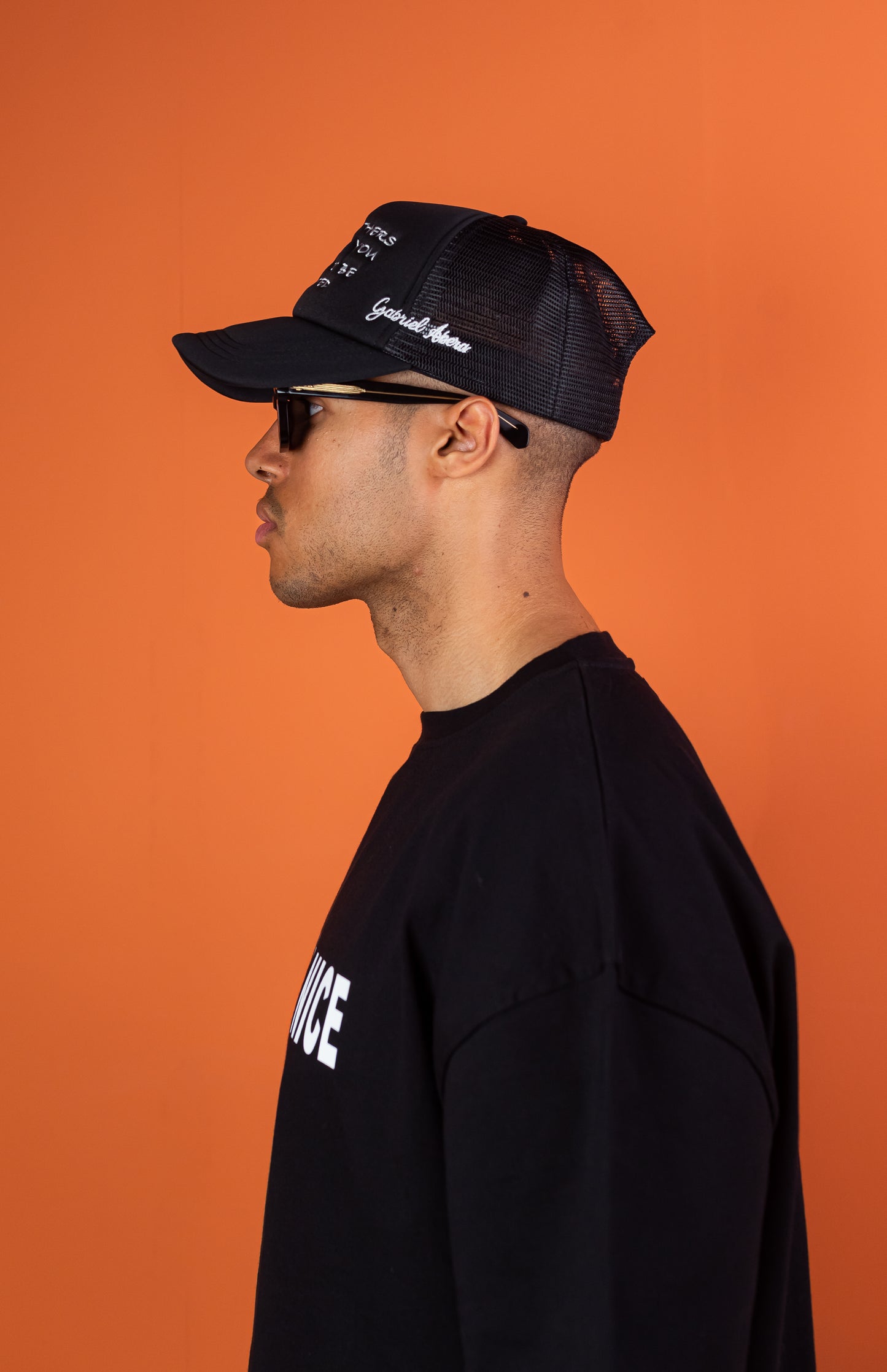 Seitennsicht eines männlichen Models, das ein schwarzes Oversize Tshirt mit der weissen Aufschrift Talk to me Nice und eine schwarze Kappe mit weisser Treat others the way you want to be threated Aufschrift trägt.