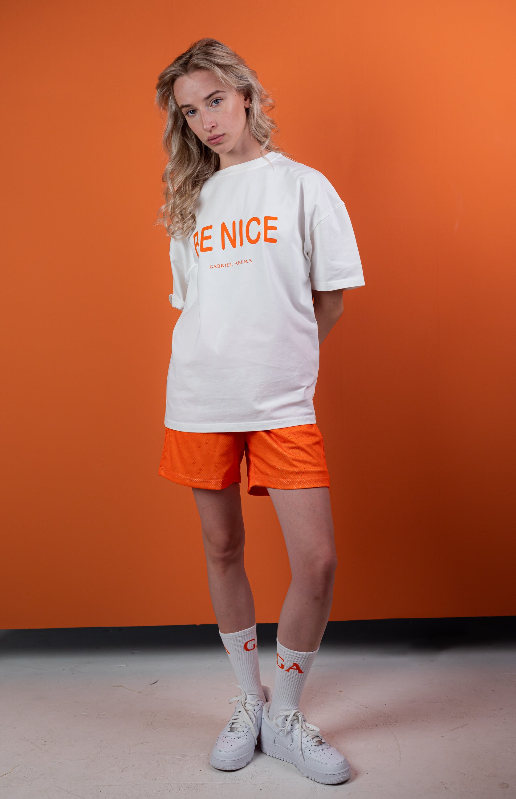 Female Model wearing White oversize tshirt with orange "be nice" print on the front 