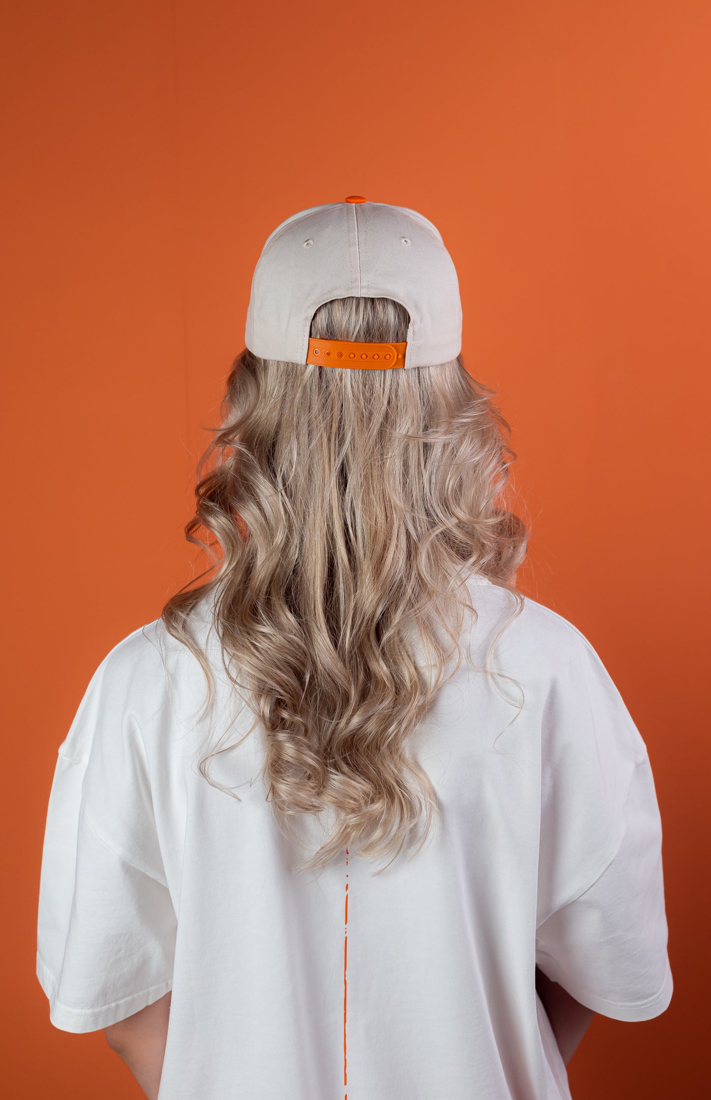Female Model wearing a White cap with orange shield with "be nice" writing on the front