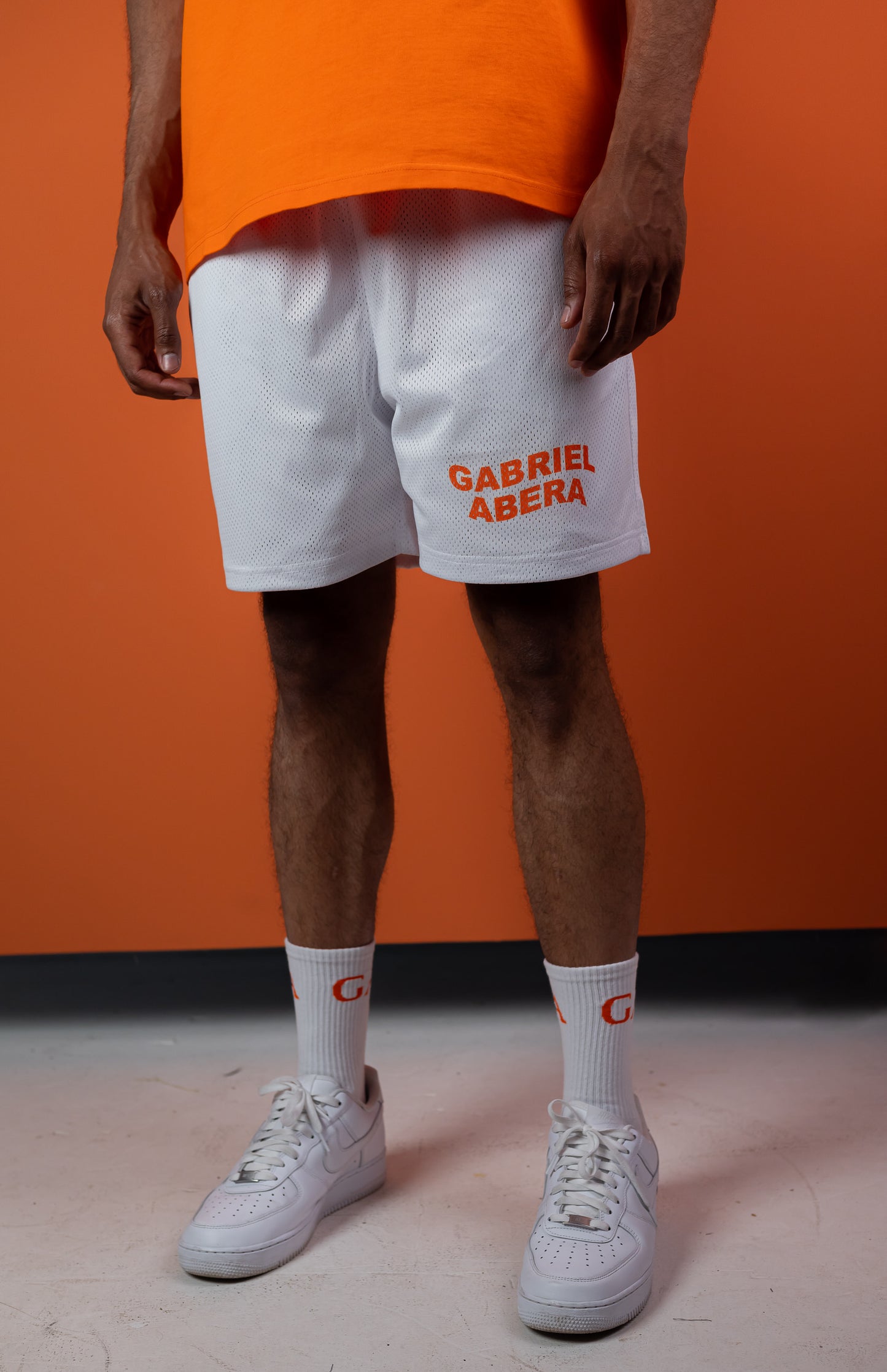 Model wearing a white mesh shorts with orange brand name print in the front