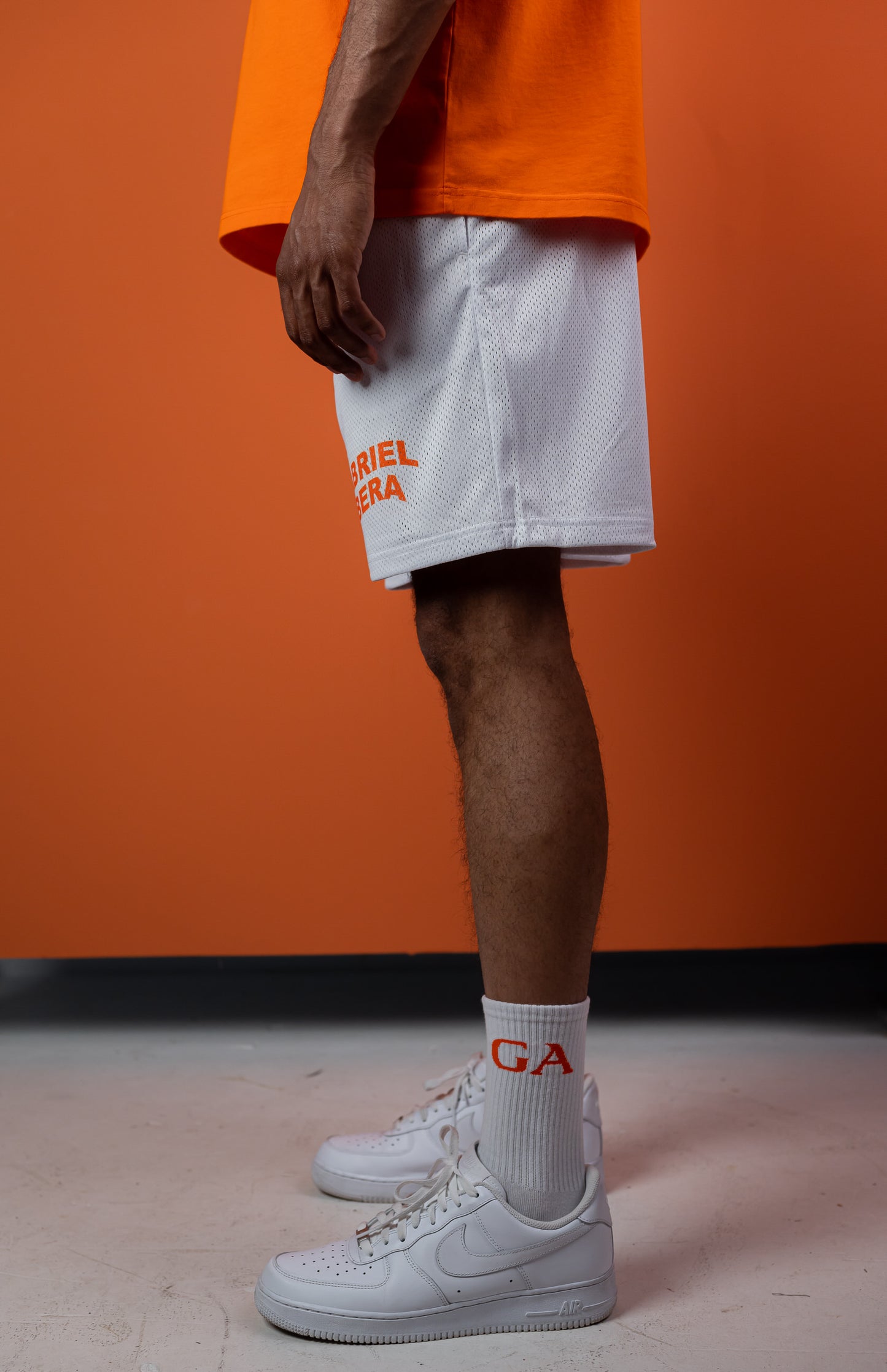 Model wearing a white mesh shorts with orange brand name print in the front