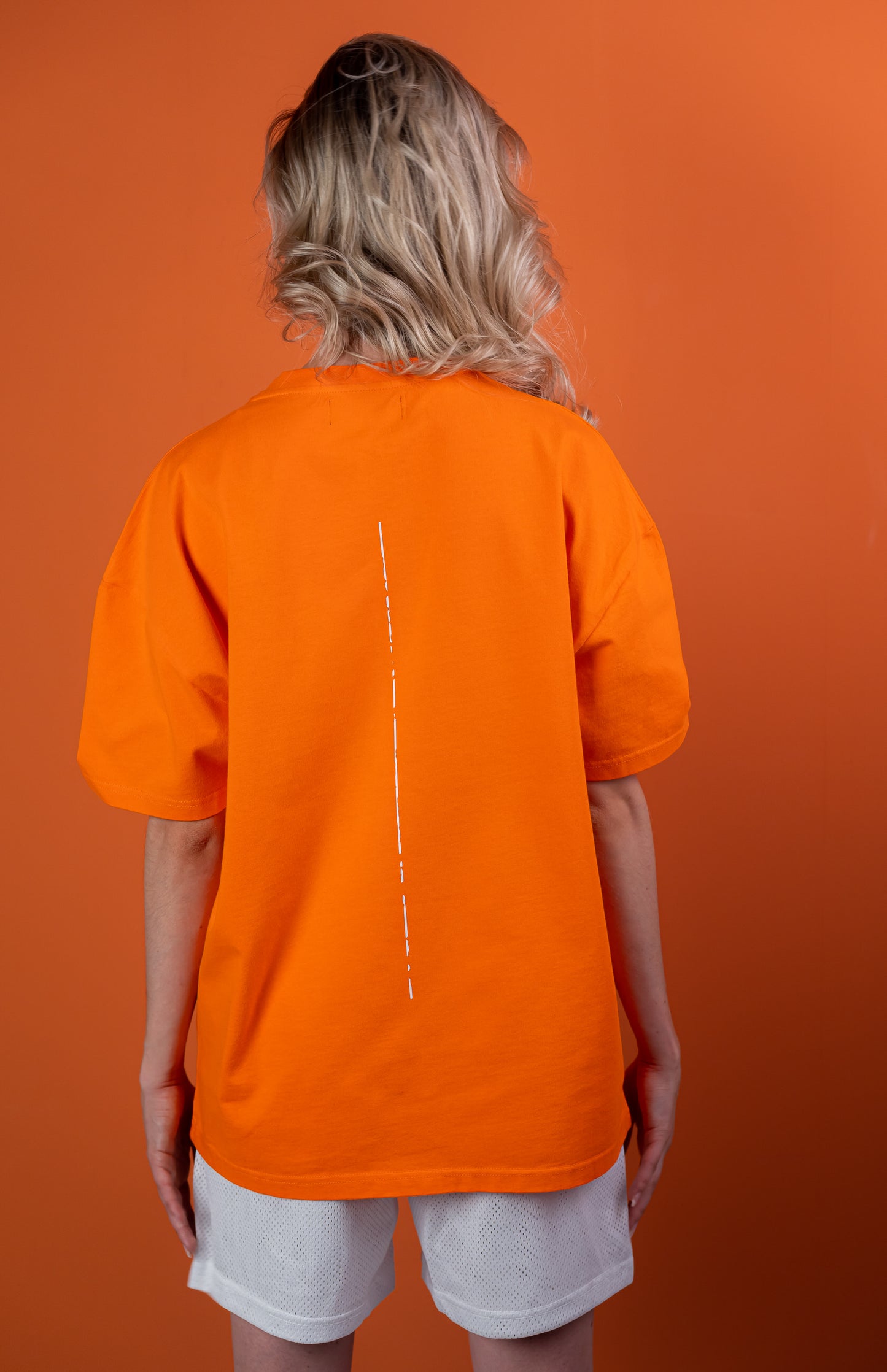 Model wearing a orange oversize tshirt with white trace on the back #