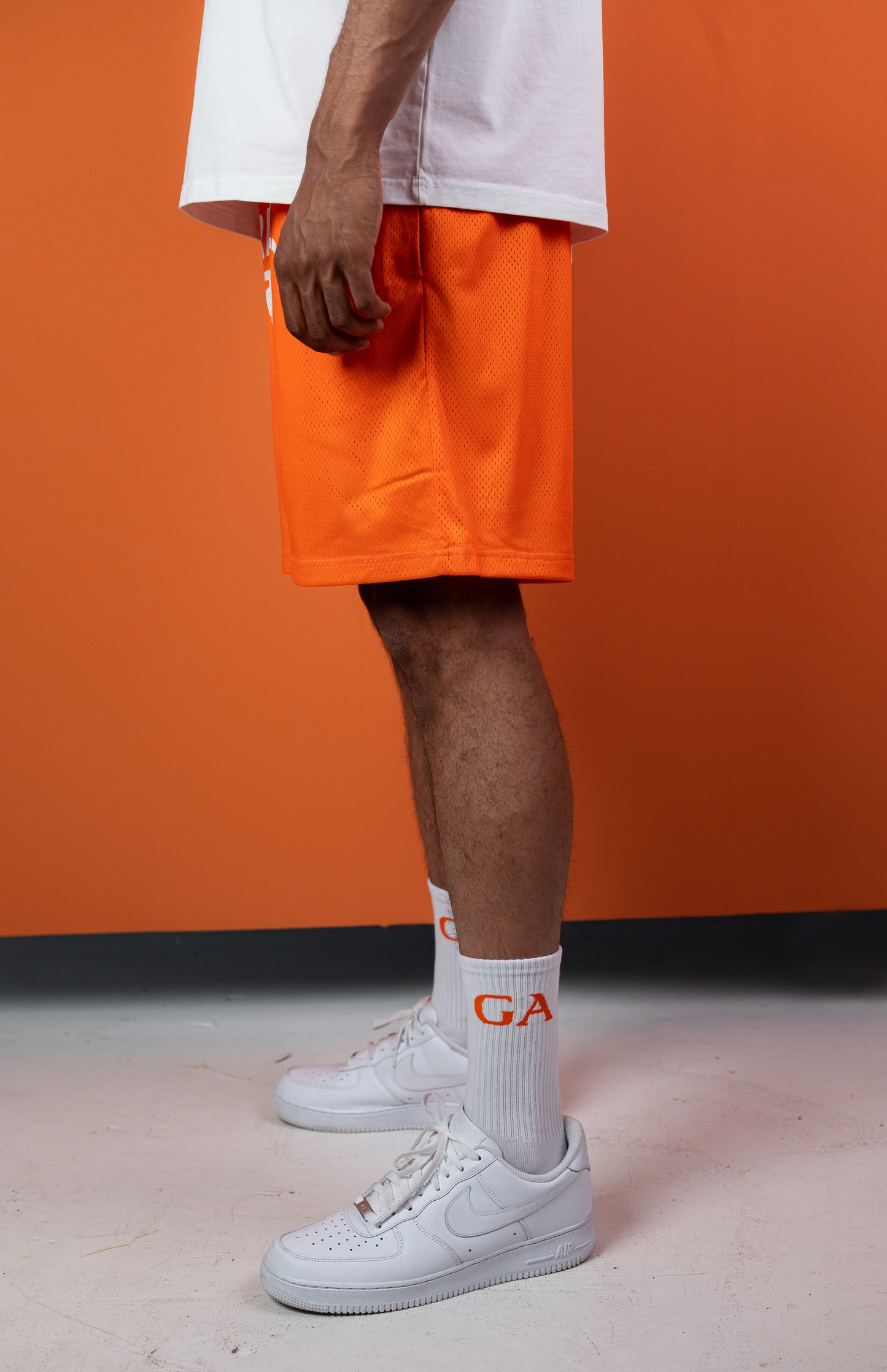 Male model wearing an Orange mesh shorts with white brand name print in the front
