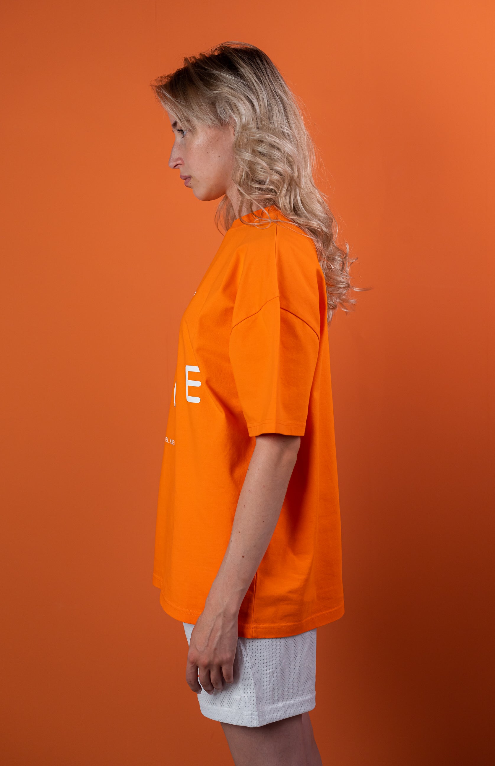 Female Model wearing Orange oversize tshirt with "be nice" print on the front 