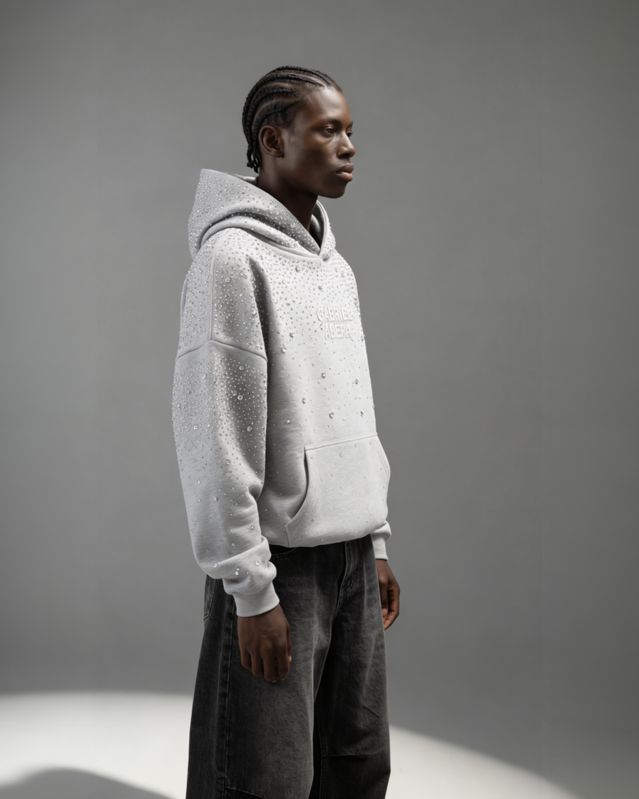 Grauer GABRIEL ABERA Universe Hoodie – männliches Model seitlich fotografiert, Oversized Silhouette mit funkelnden Rhinestones sichtbar.