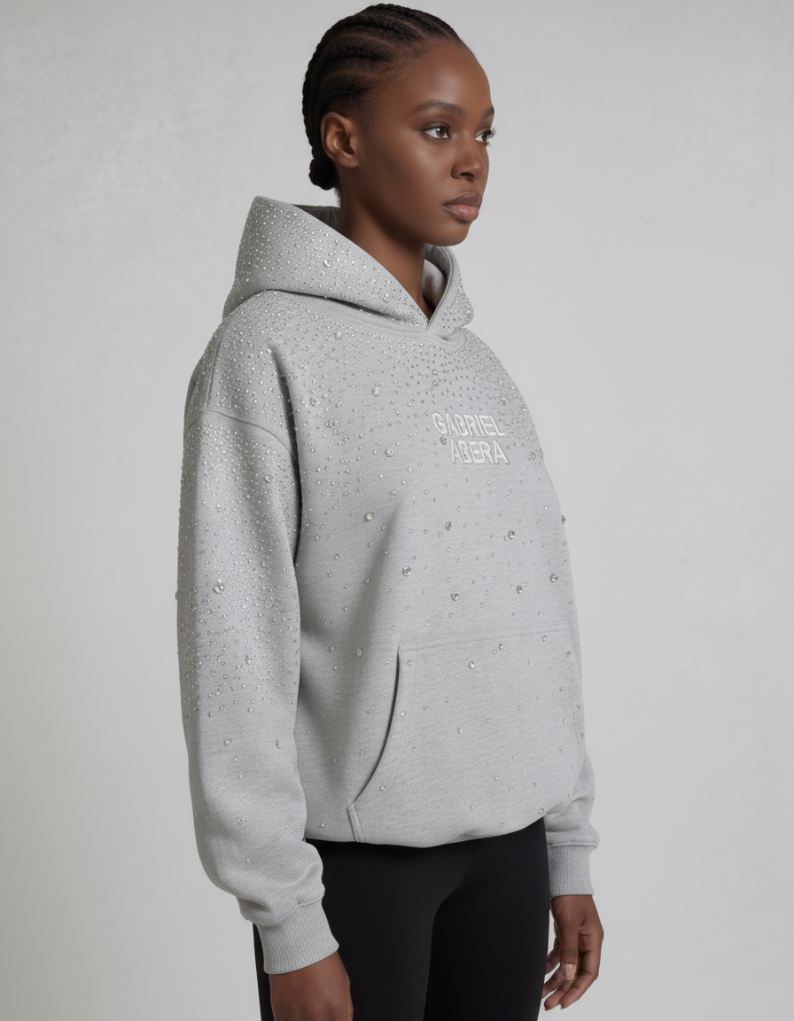 Grauer GABRIEL ABERA Universe Hoodie – weibliches Model seitlich fotografiert, Oversized Silhouette mit funkelnden Rhinestones sichtbar.