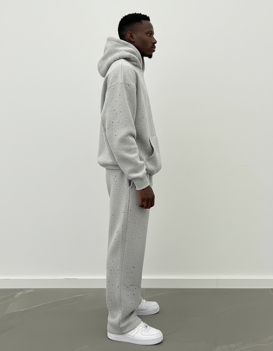 Männliches Model trägt GABRIEL ABERA splattered Tracksuit in grau mit schwarzen Farbspritzern – Sideview, Oversized Premium Streetwear Fashion