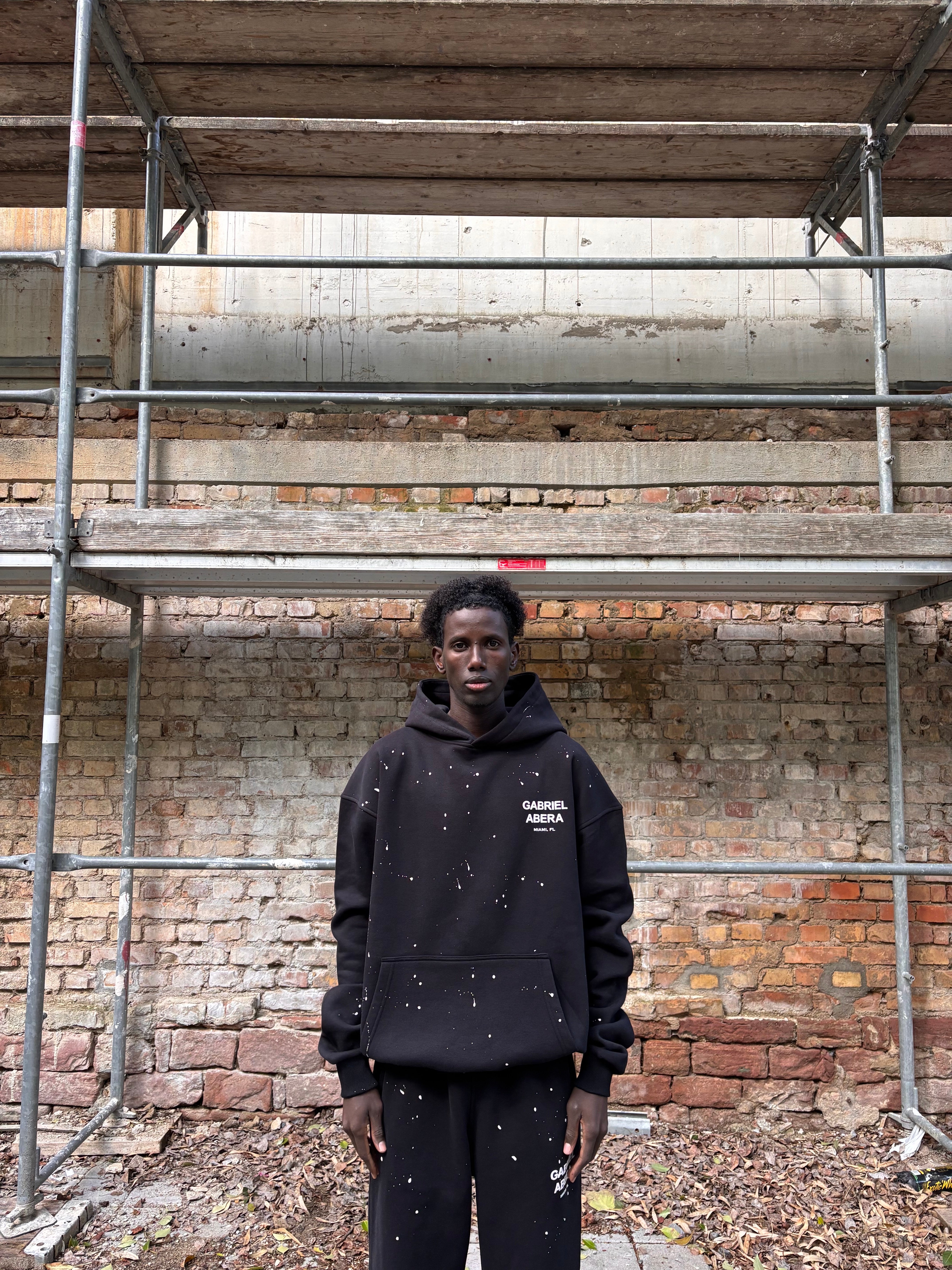 Model trägt GABRIEL ABERA Splattered Puff Hoodie Black/White – Frontansicht, Oversized Fit mit handgemachtem Farbspritzer-Design.