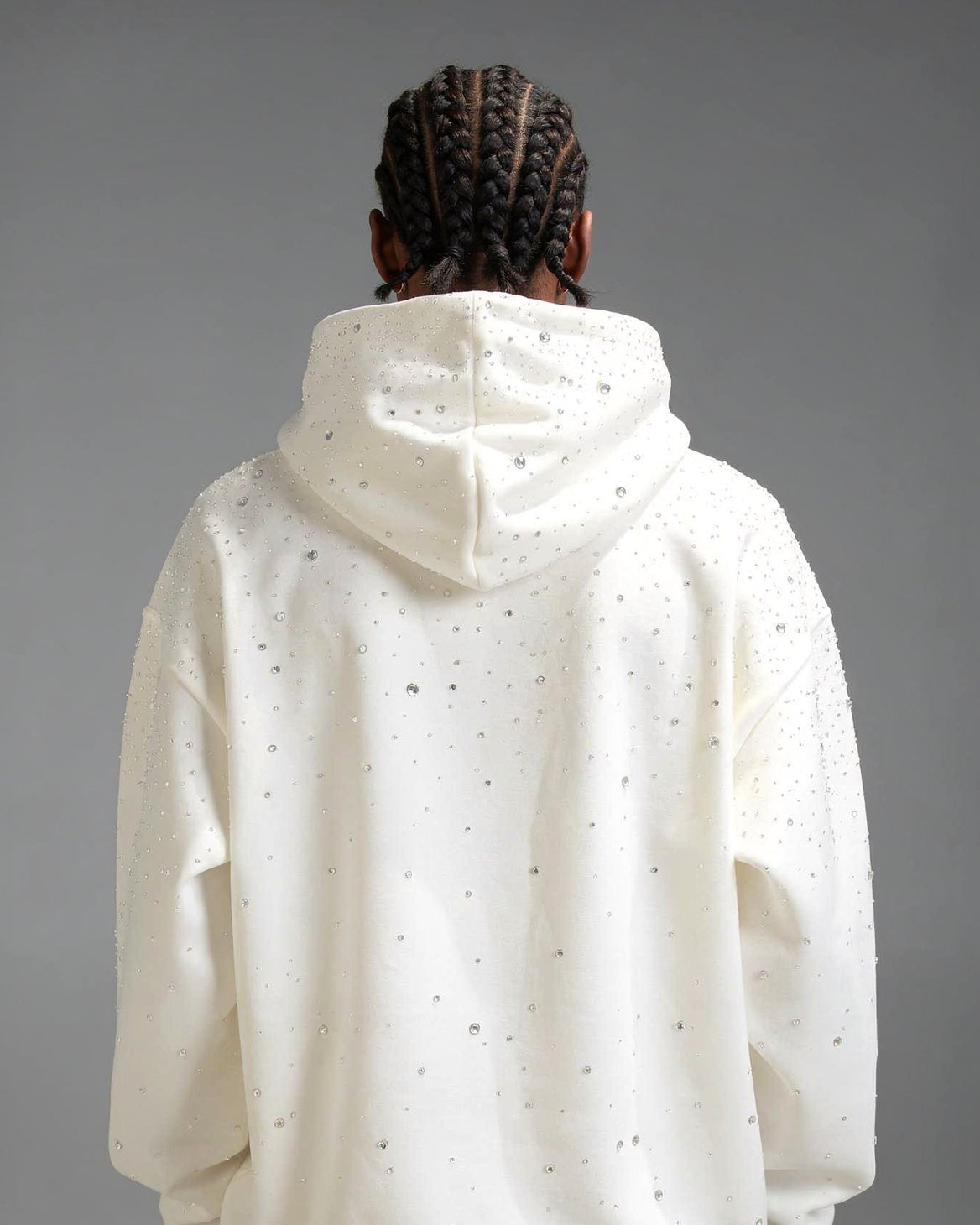 Model trägt Rhinestone Hoodie in cream weiß von Gabriel Abera. Die Ansicht ist von hinten.