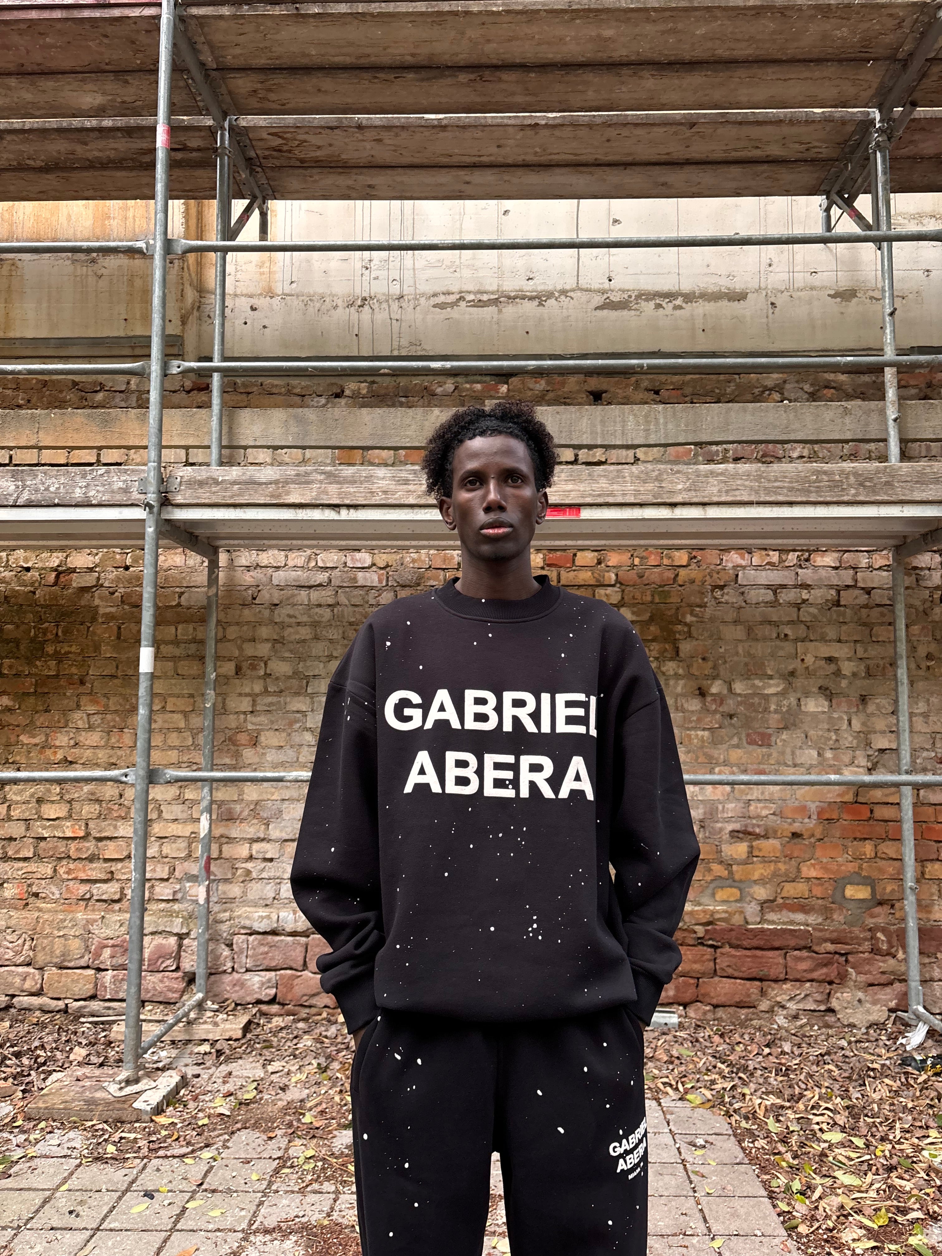Model trägt GABRIEL ABERA Splattered Puff Sweater Black/White – Vorderansicht im Streetwear Style mit Oversized Schnitt.