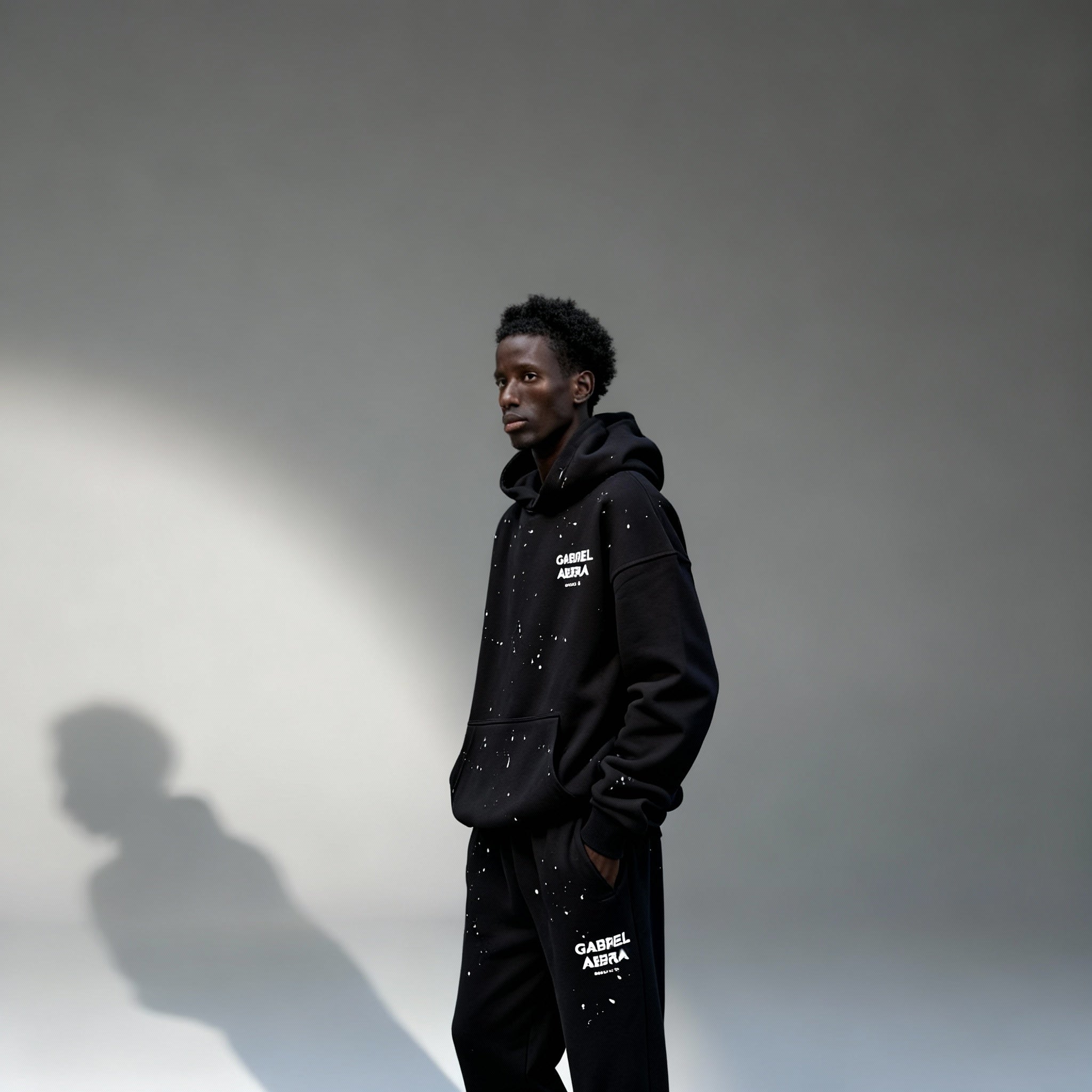 Model trägt GABRIEL ABERA Splattered Puff Hoodie Black/White – Seitenansicht, lockerer Oversized Fit und künstlerisches Paint Splatter Design.