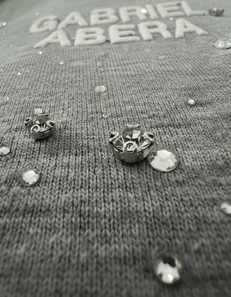 Nahaufnahme des grauen GABRIEL ABERA Rhinestone Hoodie – handgesetzte Steine funkeln, hochwertige Textur, Fashion Detailshot.